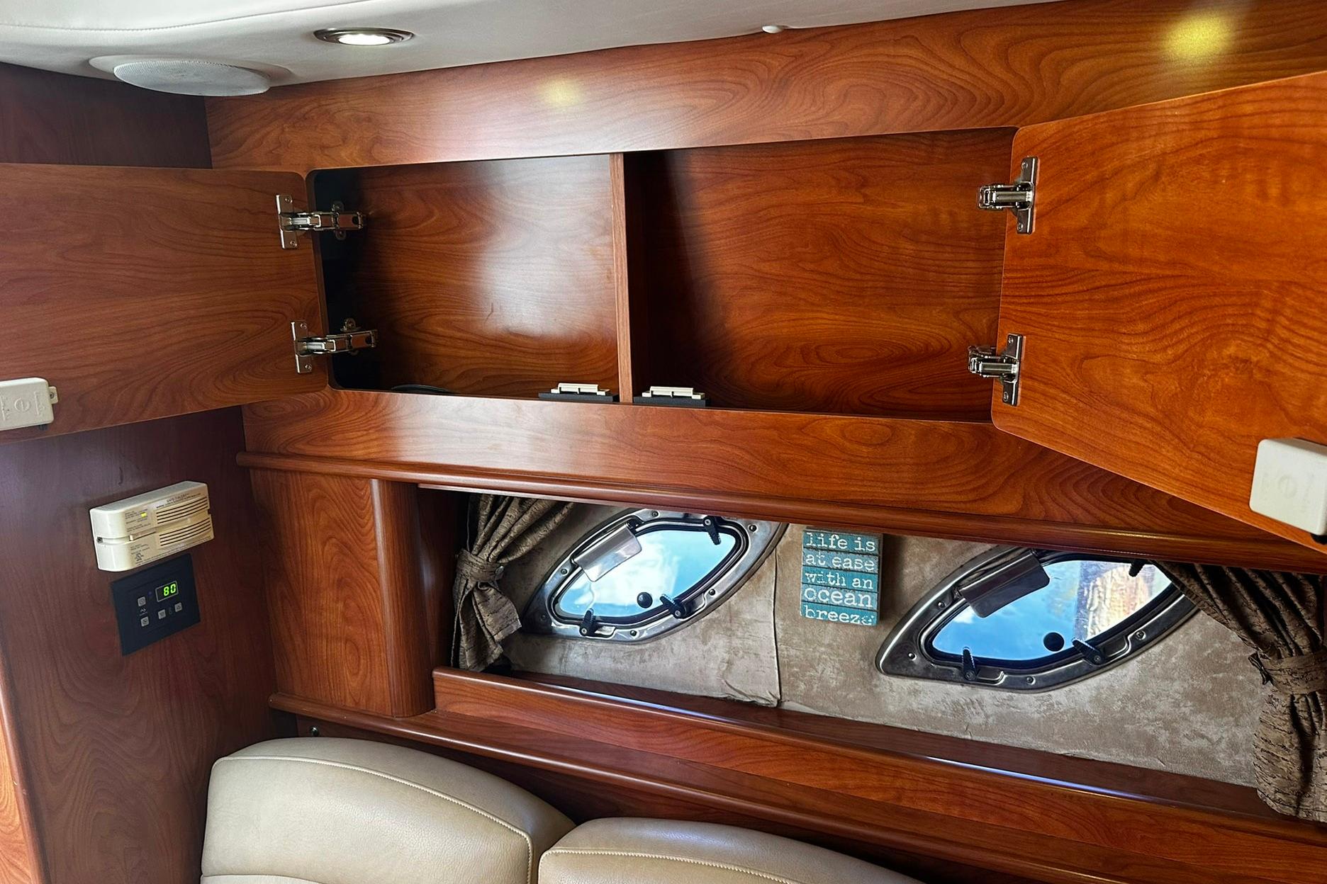 Interior of 2012 Rinker 310 Express Cruiser LE with wooden cabinets and porthole windows.