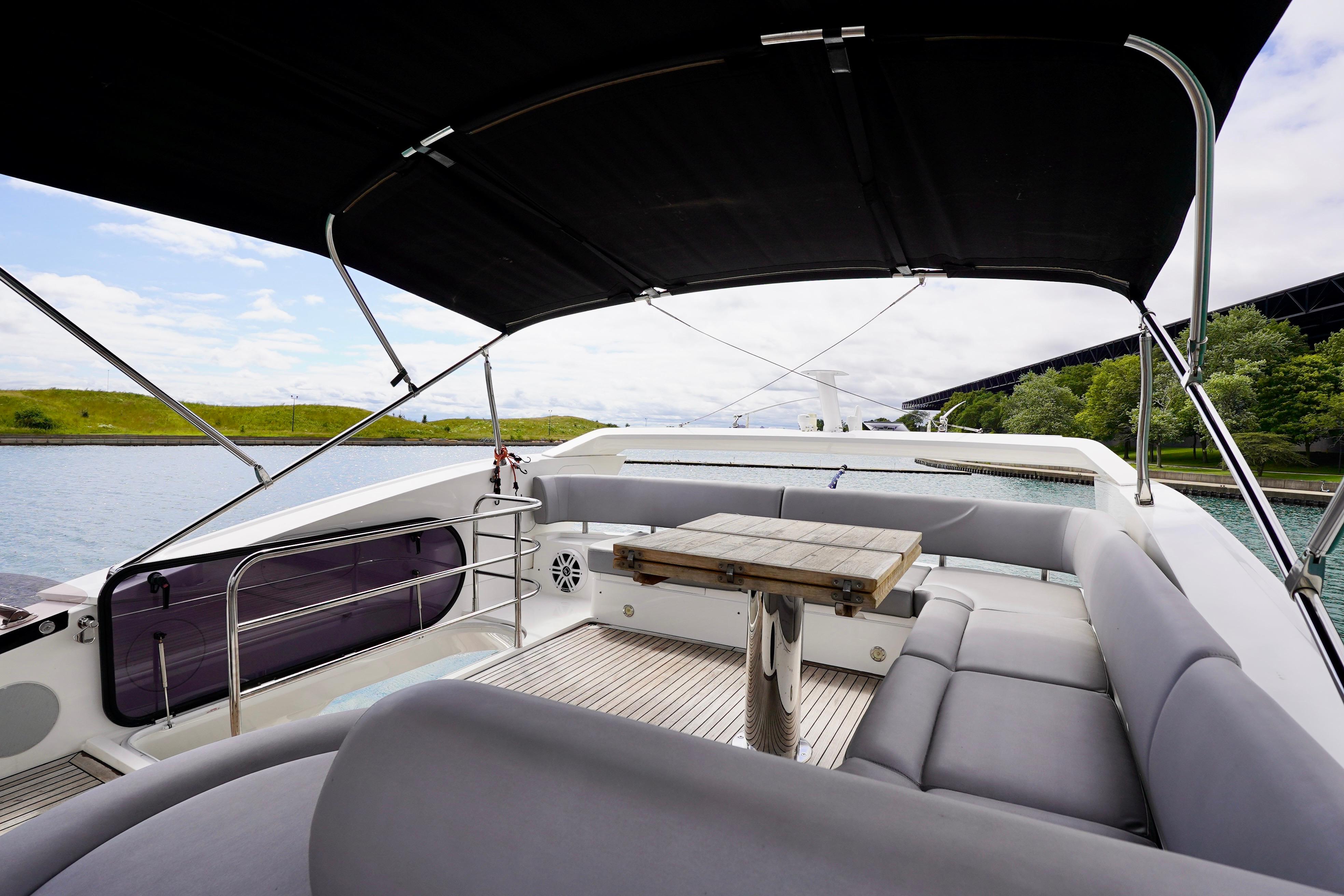Luxurious 2019 Sunseeker Manhattan 66 yacht deck with seating and table, under canopy.