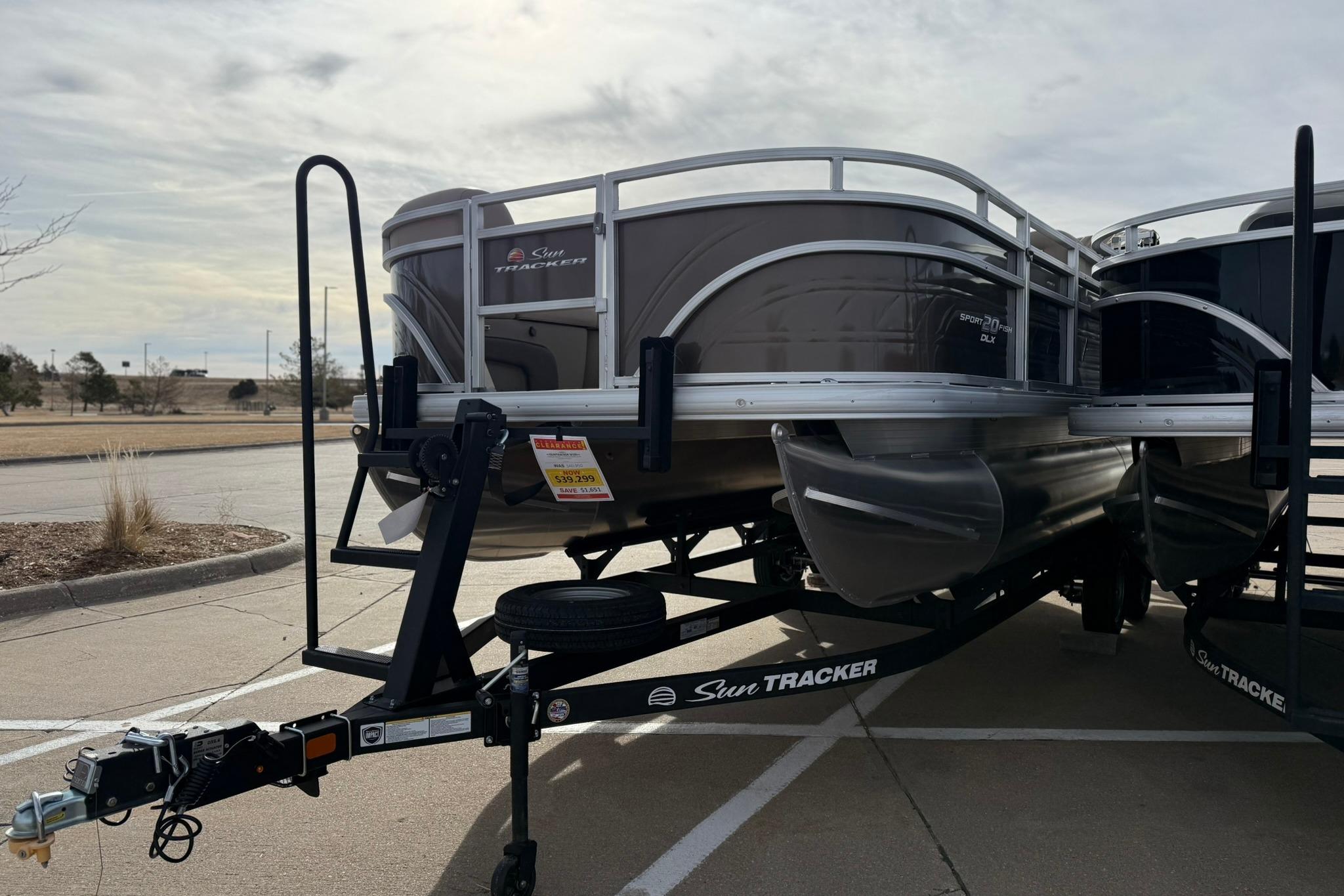 2025 Sun Tracker SportFish 20 DLX pontoon boat on trailer in parking lot.