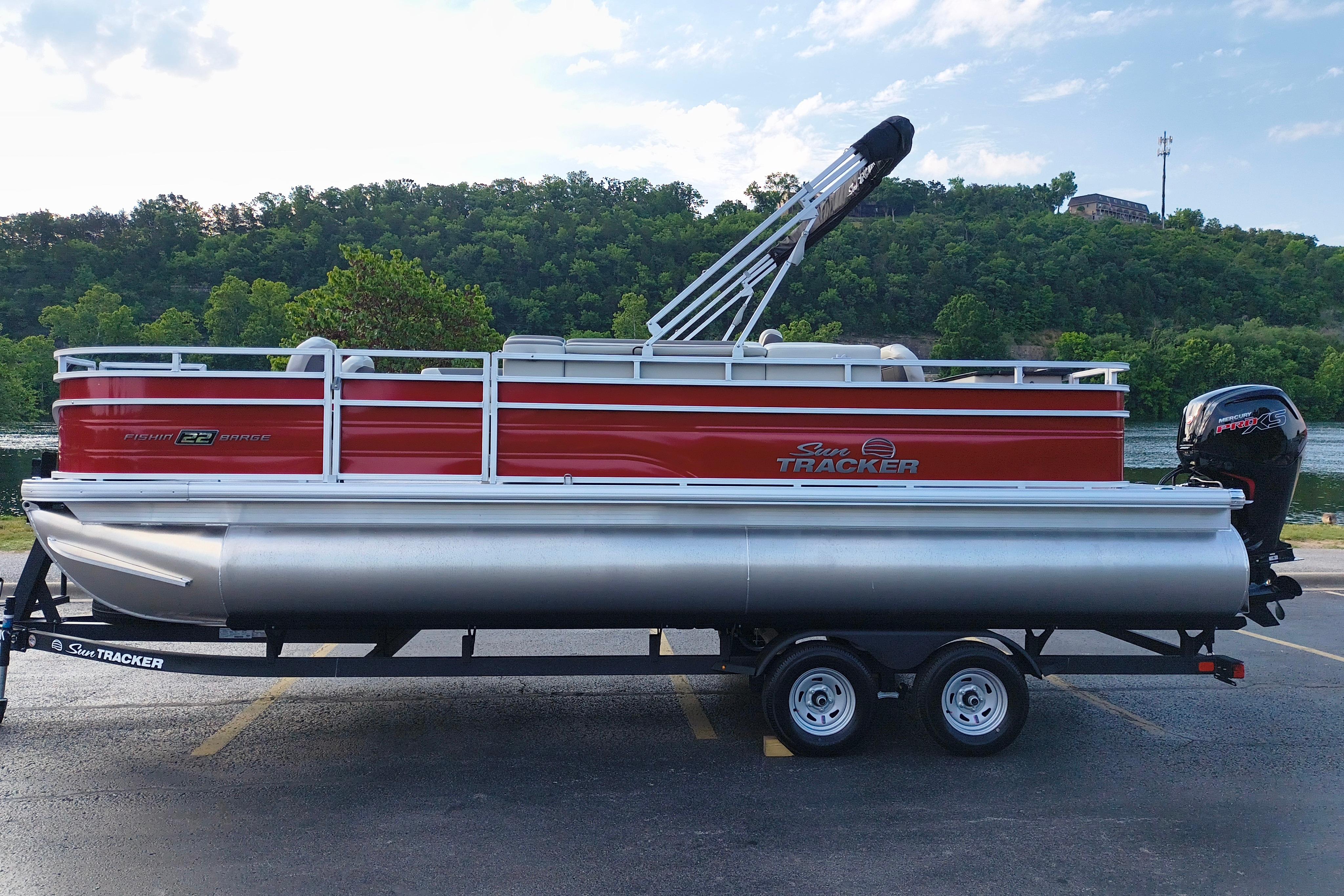 2026 Sun Tracker Fishin' Barge 22 DLX pontoon boat on trailer, parked near a scenic river.
