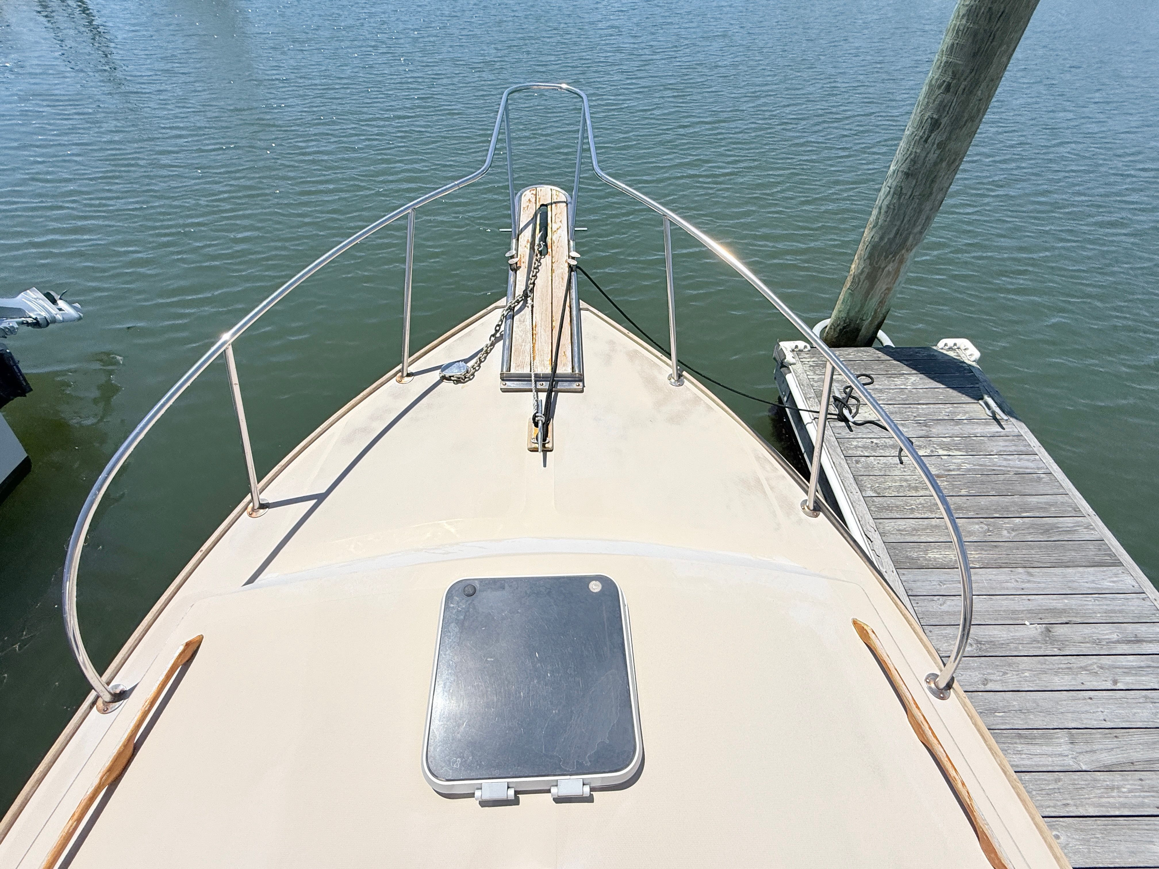 Bow of a 1989 Fortier 26 boat docked at a wooden pier on the water.