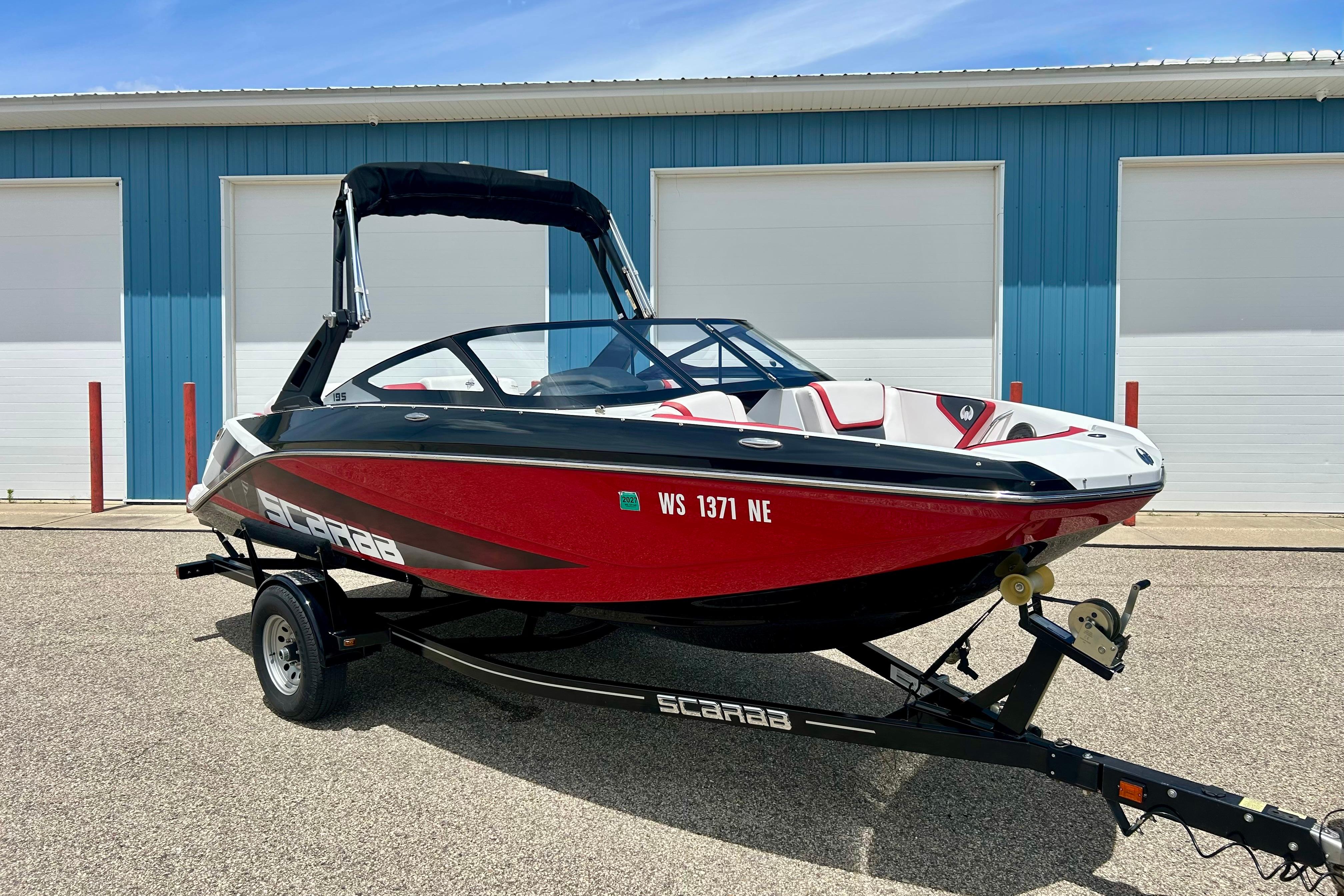2021 Scarab 195 ID boat in red and black, parked on a trailer outside a blue building.