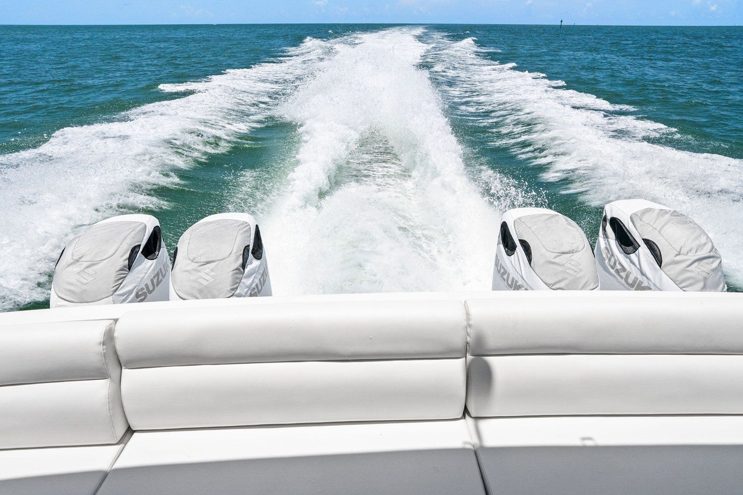 Four outboard engines propel a catamaran across open sea, leaving a white wake.