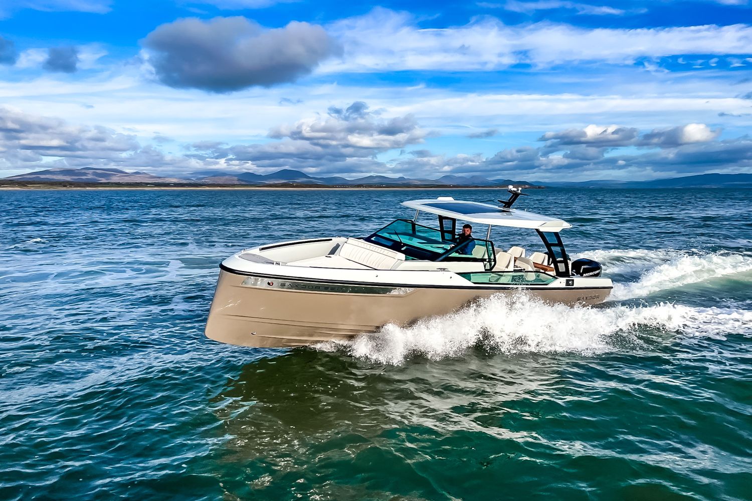A Saxdor SX320 GTO boat speeds across the water under a blue sky.