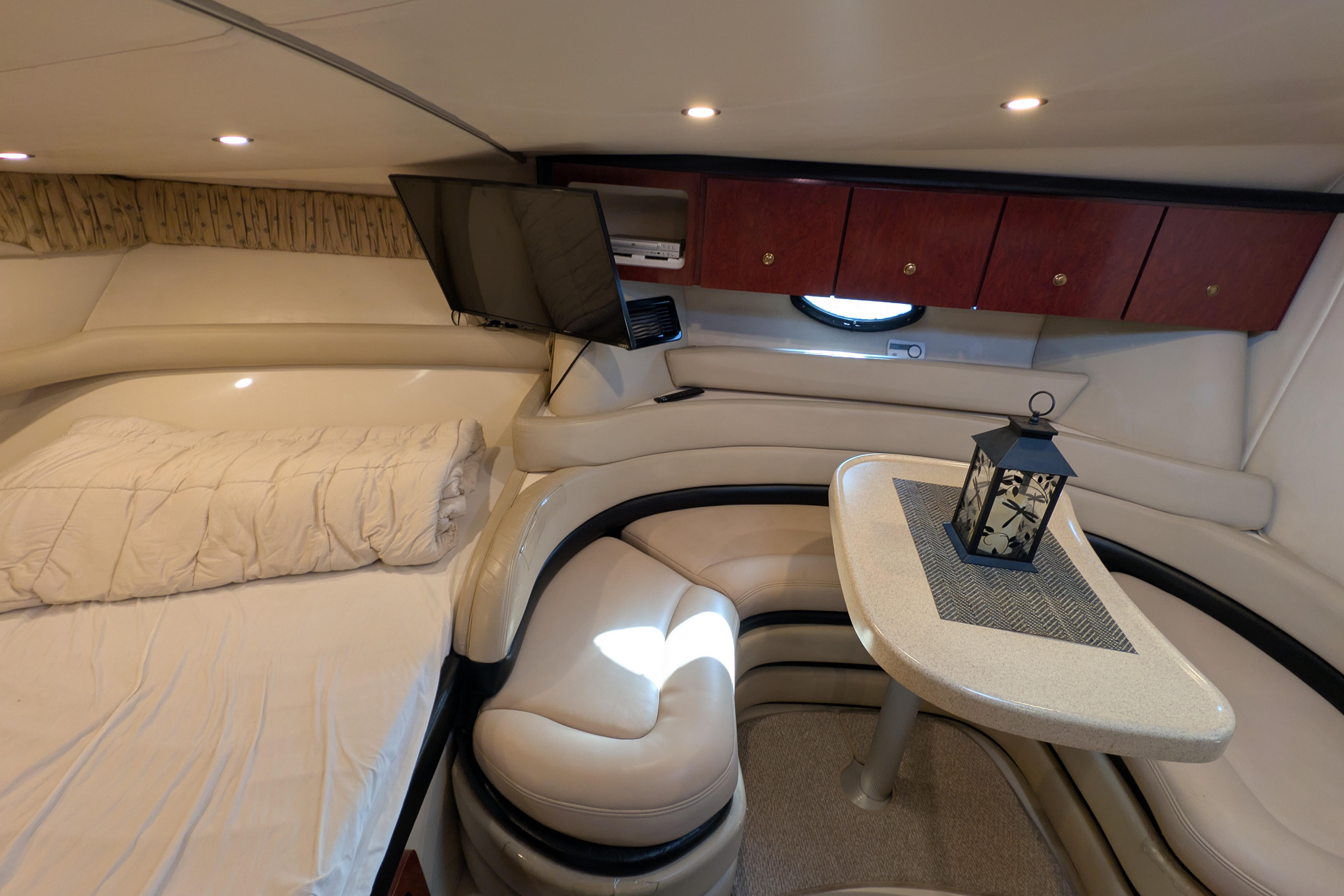 2001 Wellcraft 3300 Martinique cabin interior with cozy seating, table, and ambient lighting.