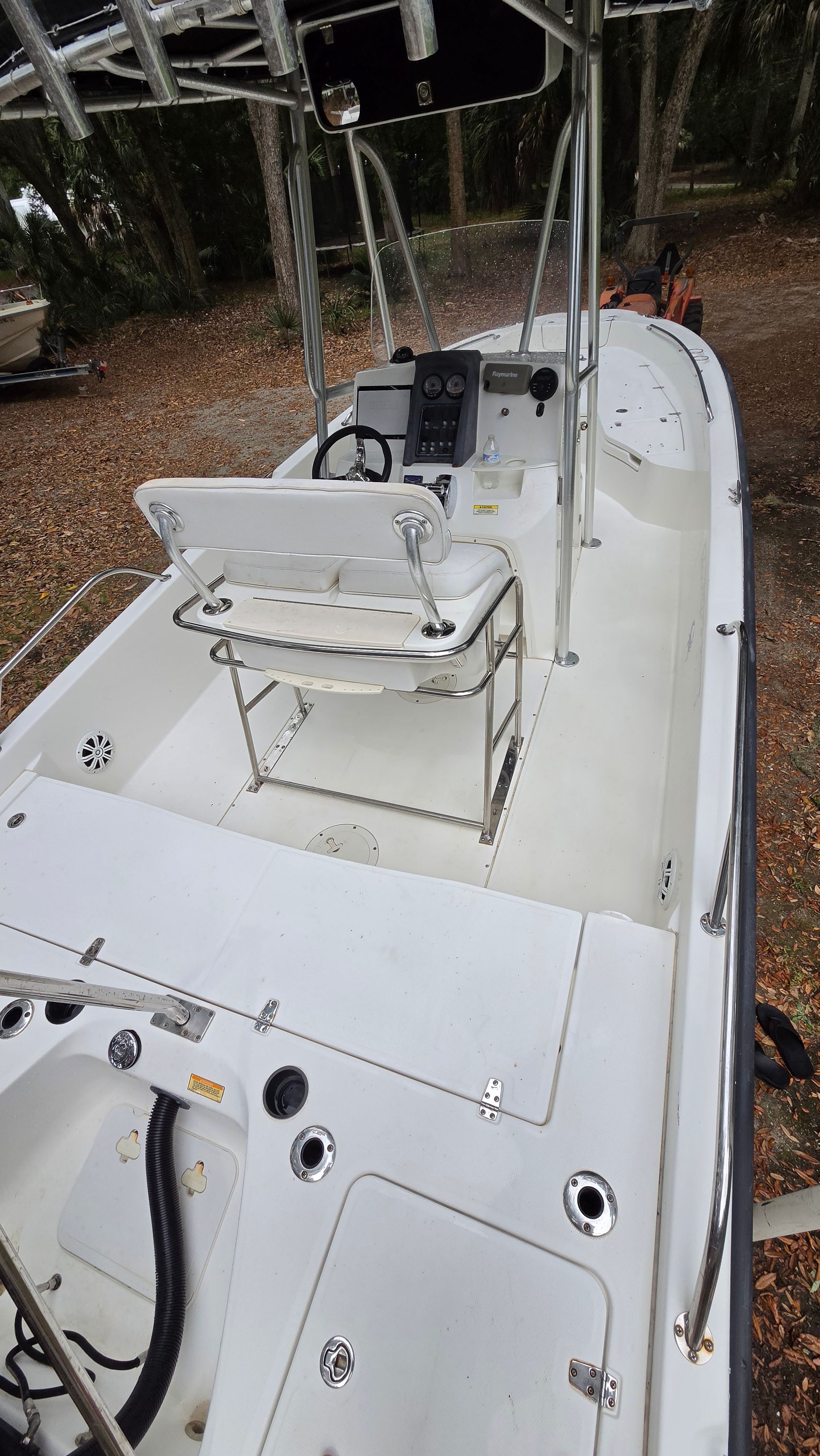 A 2008 Boston Whaler 230 Dauntless with a white deck and helm console, parked on dry leaves.