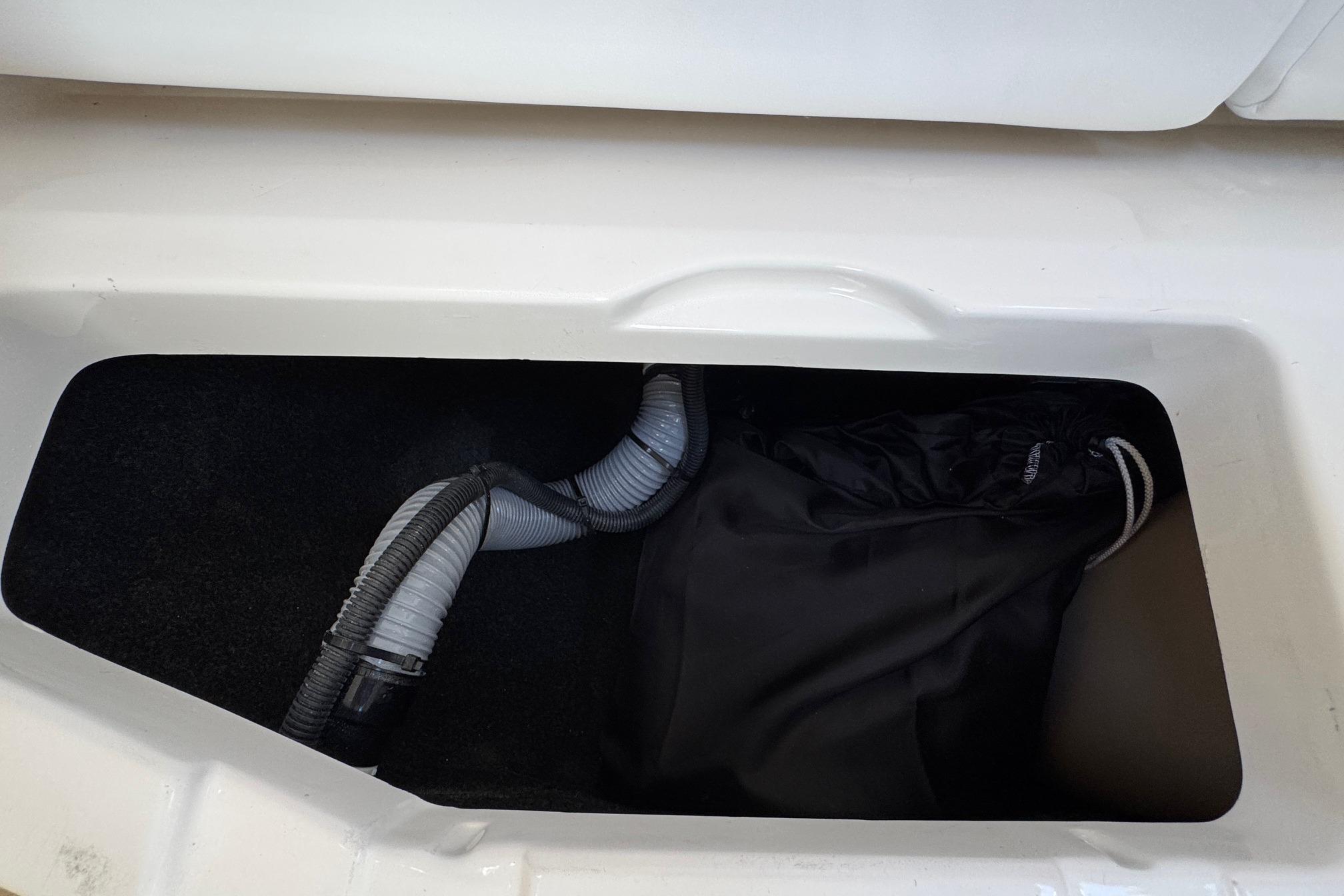 Storage compartment in 2026 Regal 33 XO boat with hoses and black bag.