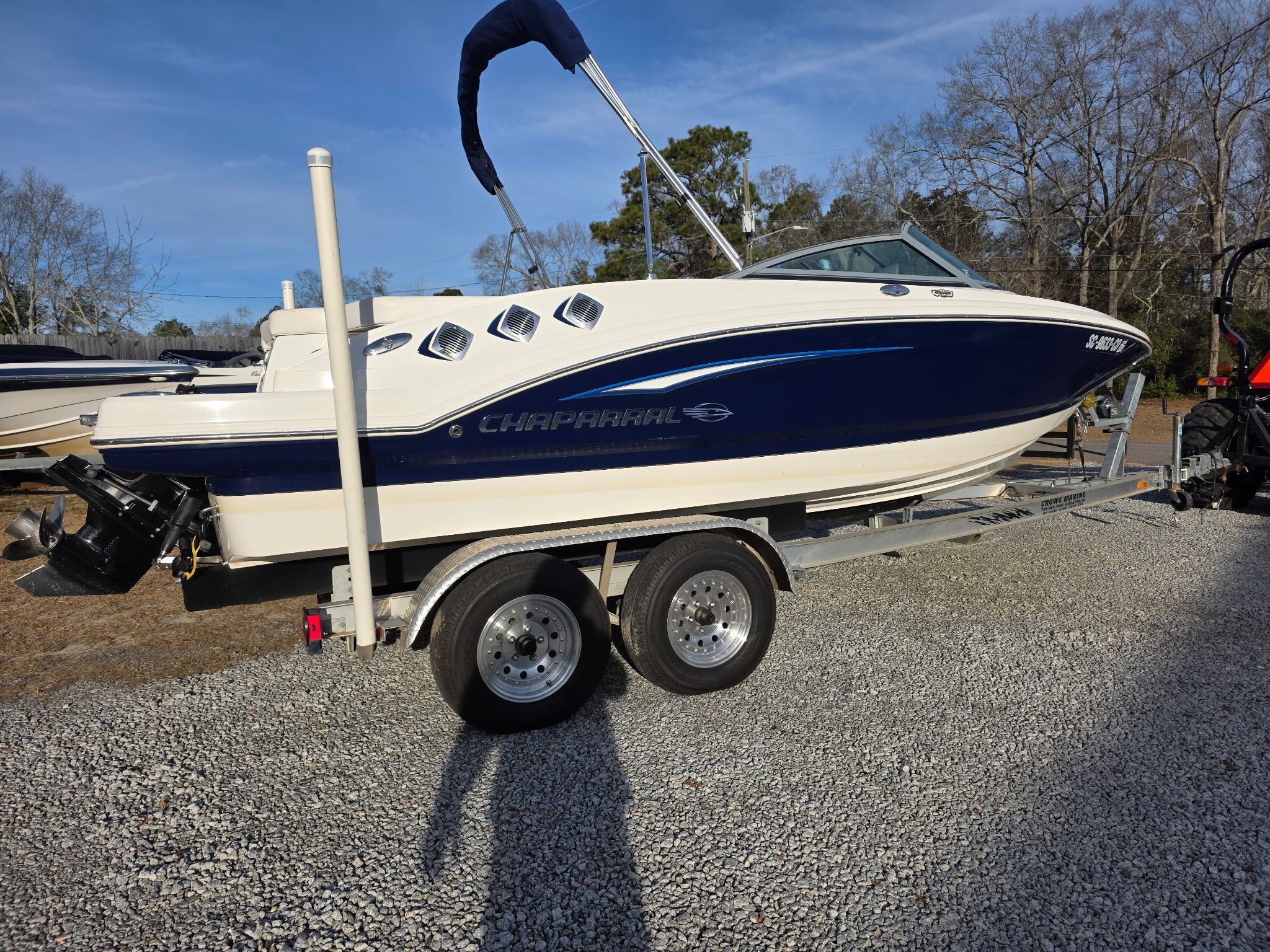 A Chaparral 206 SSi boat on a trailer, parked on a gravel lot.
