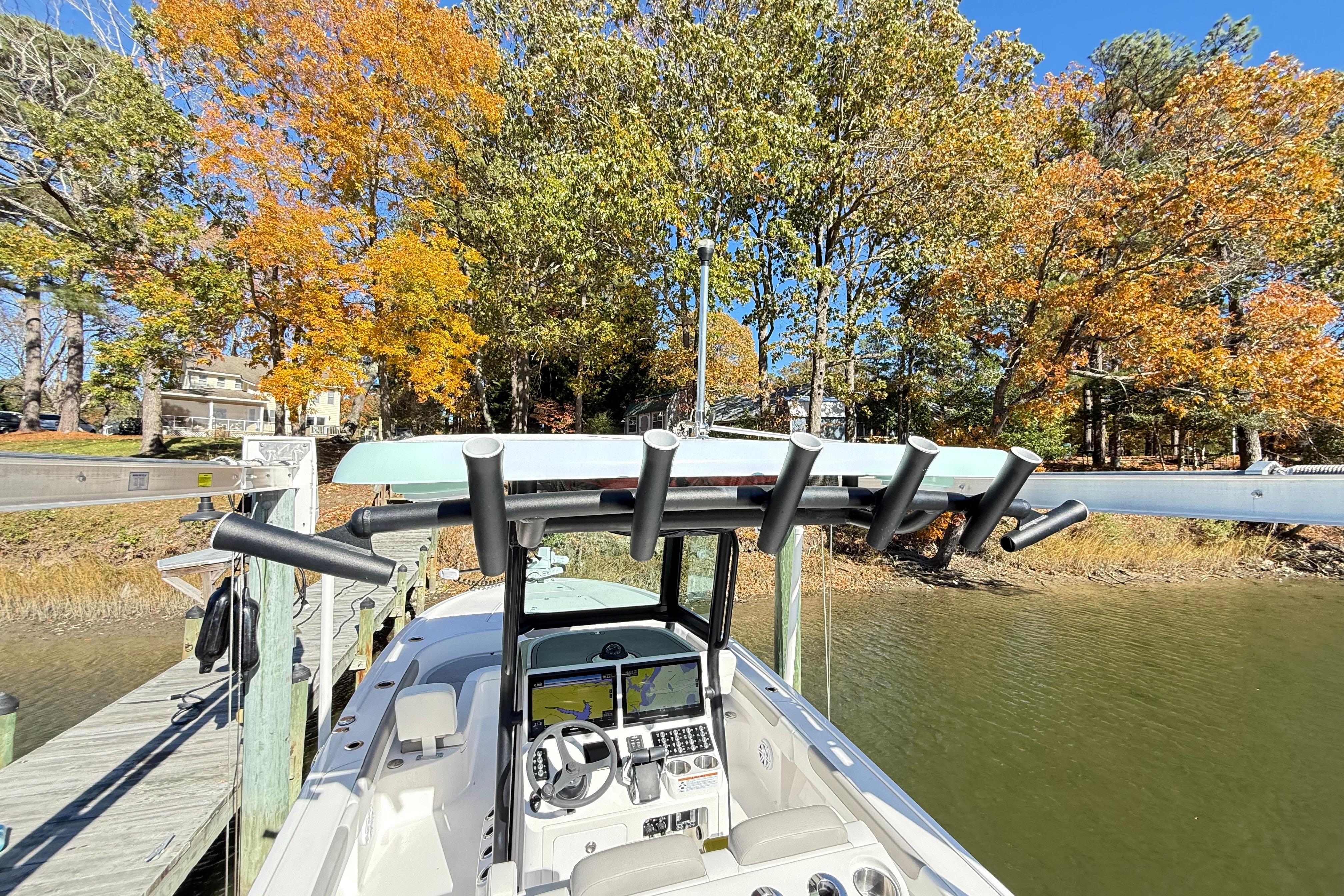2023 Caymas 281 HB boat docked by autumn trees, showcasing helm and rod holders.