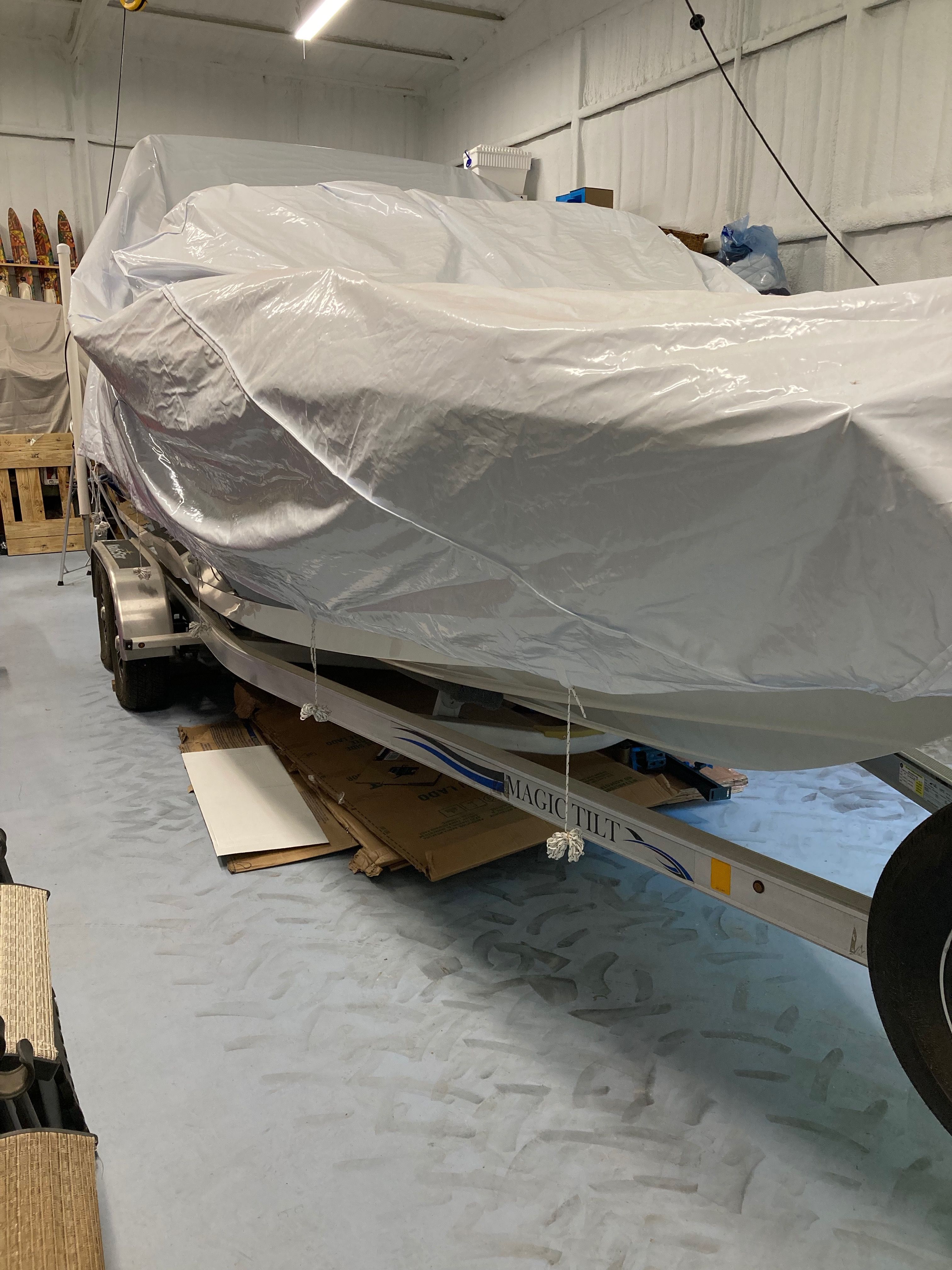 A boat on a trailer, covered with a tarp, inside a storage area.