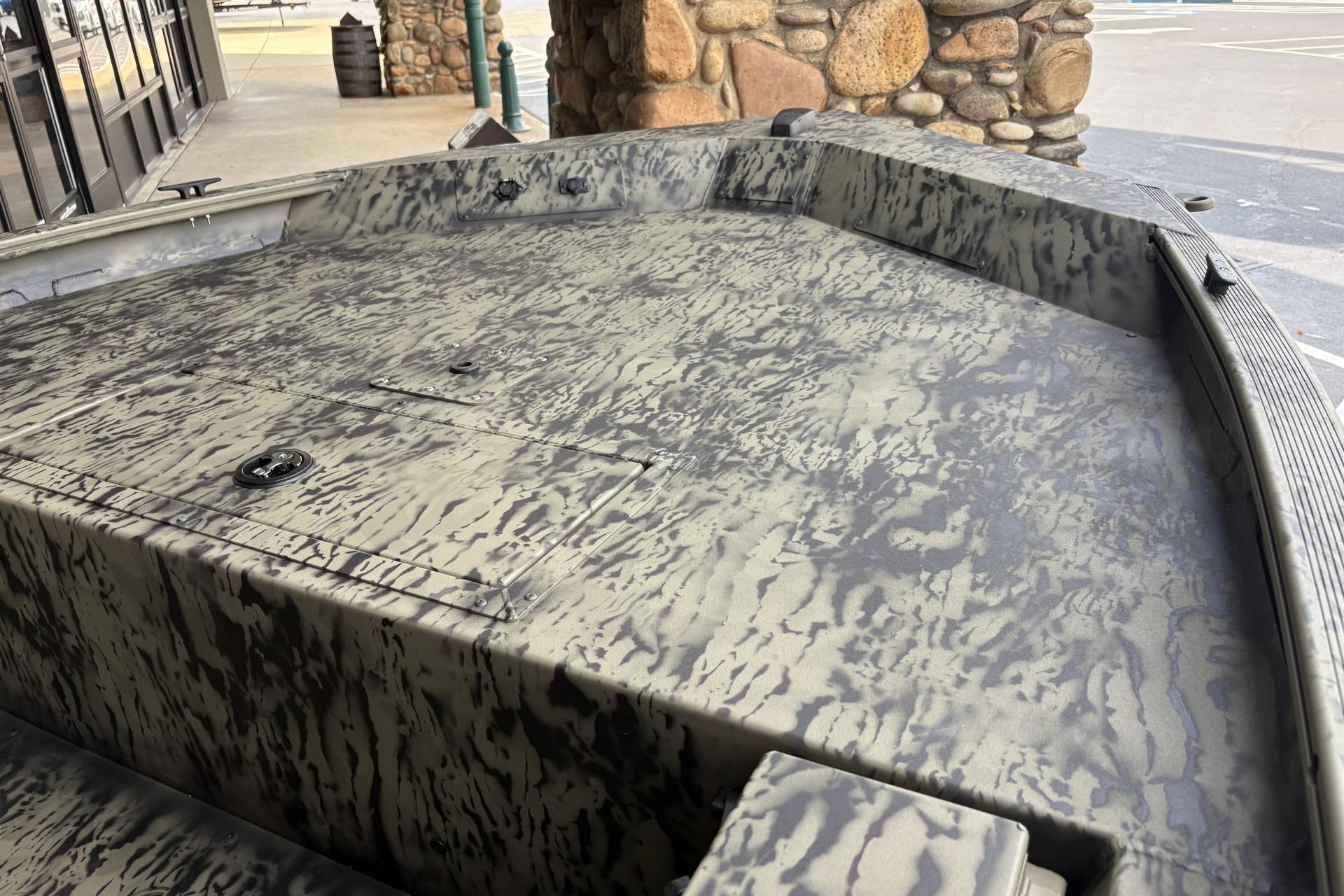 2026 Tracker Grizzly 1654 T Sportsman boat with camouflage pattern, docked near stone wall.