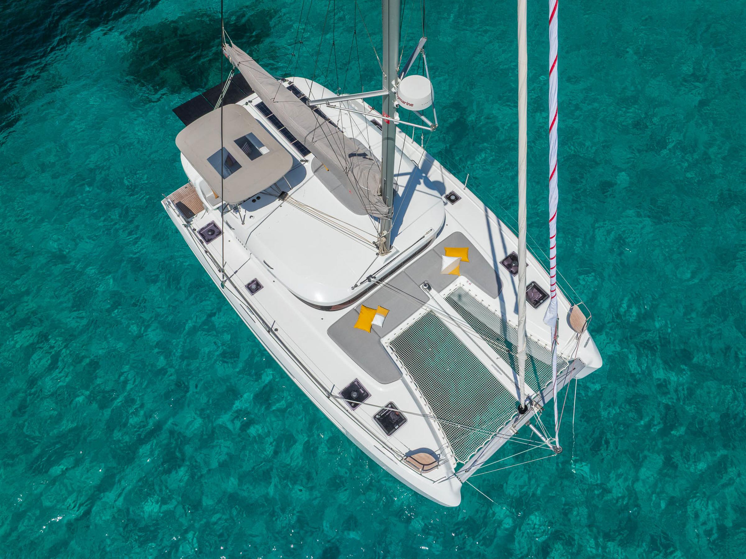 Aerial view of 2025 Lagoon 38 catamaran sailing on clear turquoise water.