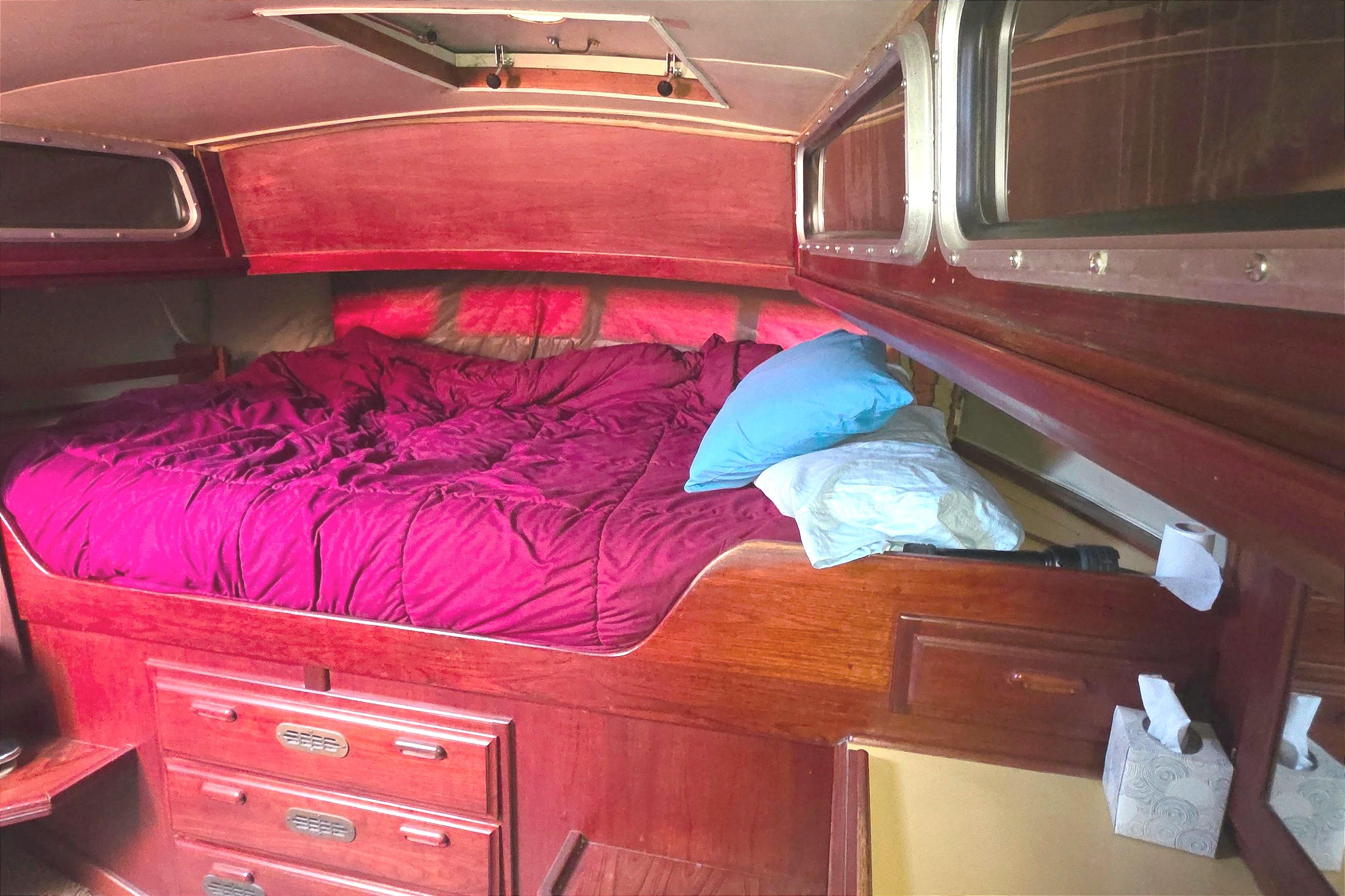 Cozy cabin interior of 1978 Islander Freeport 41 sailboat with red bedding and wooden furnishings.