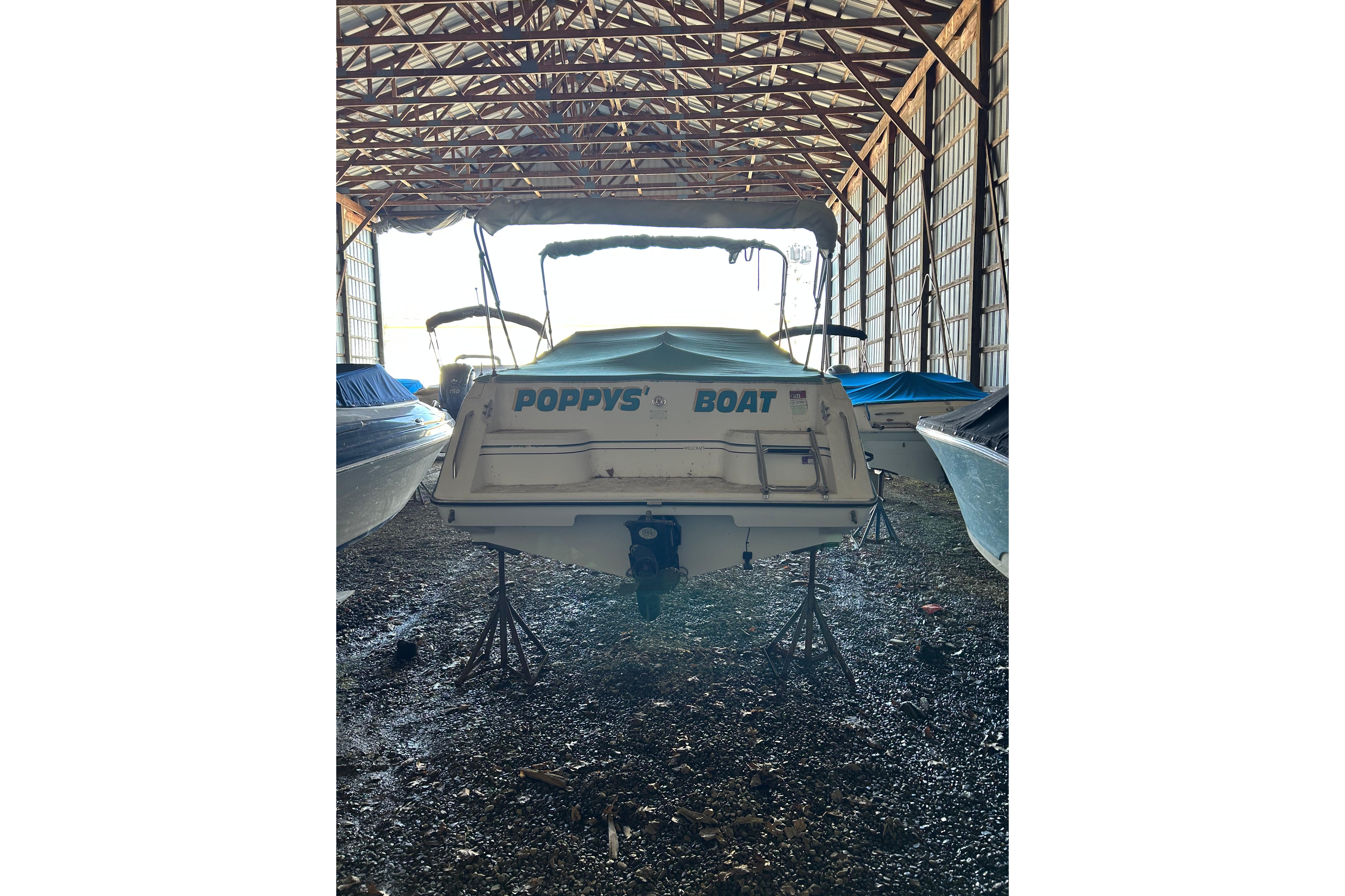 1991 Wellcraft 232 Eclipse boat named "Poppy's Boat" stored in a covered facility.