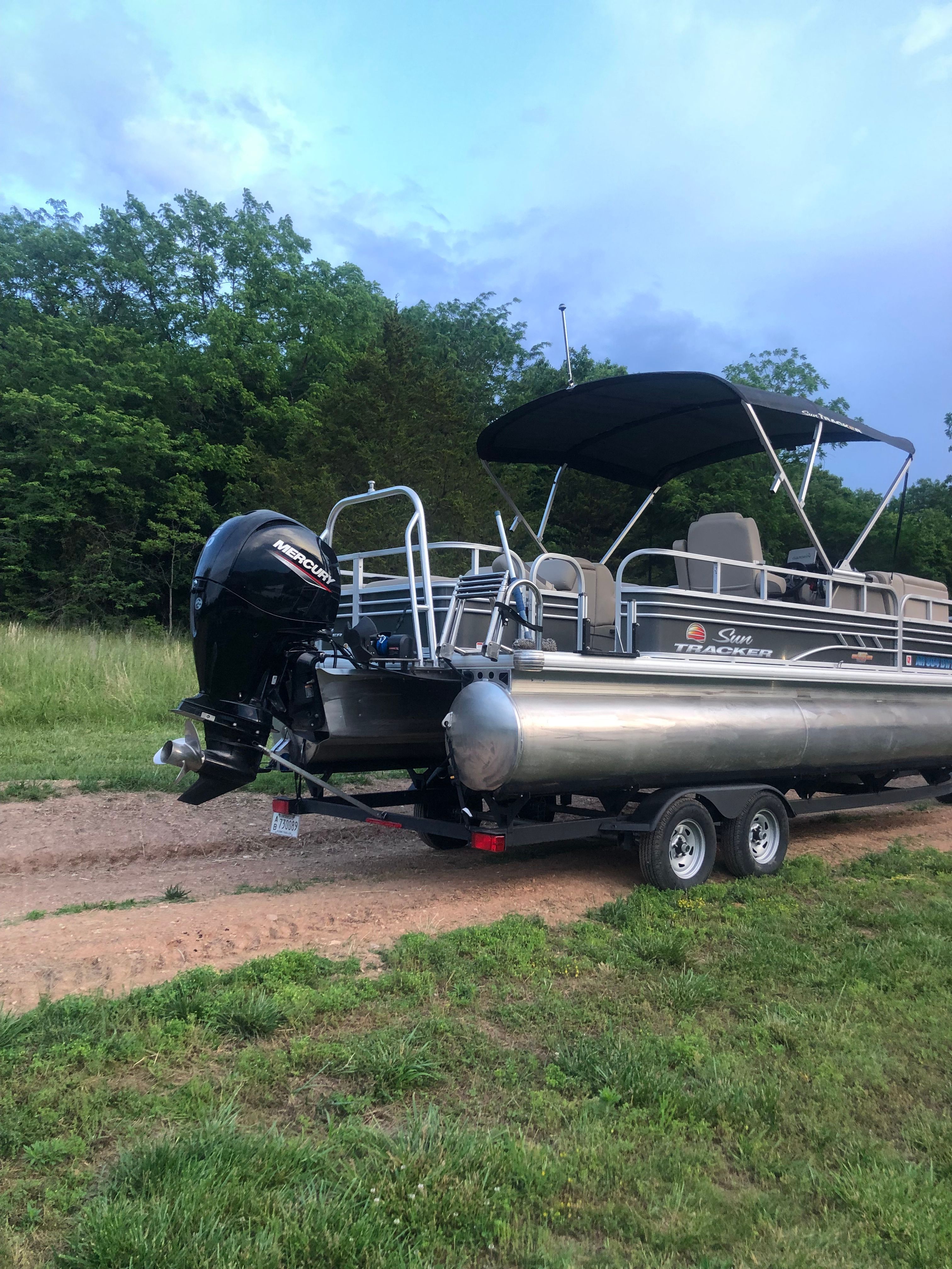 A 2023 Sun Tracker Fishin' Barge 22 DLX on a trailer in a green setting.