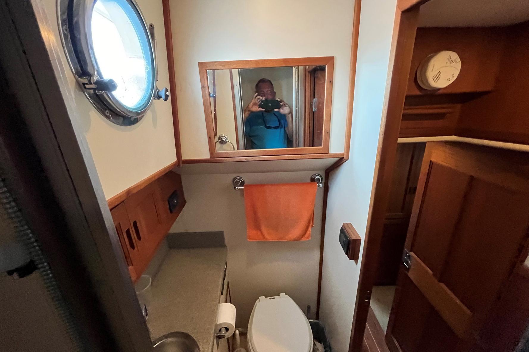 Bathroom interior of 2007 Nordic Tug 42 with porthole and wooden cabinetry.