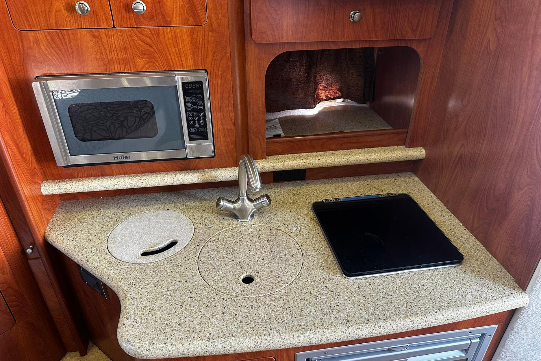 2012 Rinker 310 Express Cruiser LE kitchen with microwave, sink, and cooktop.