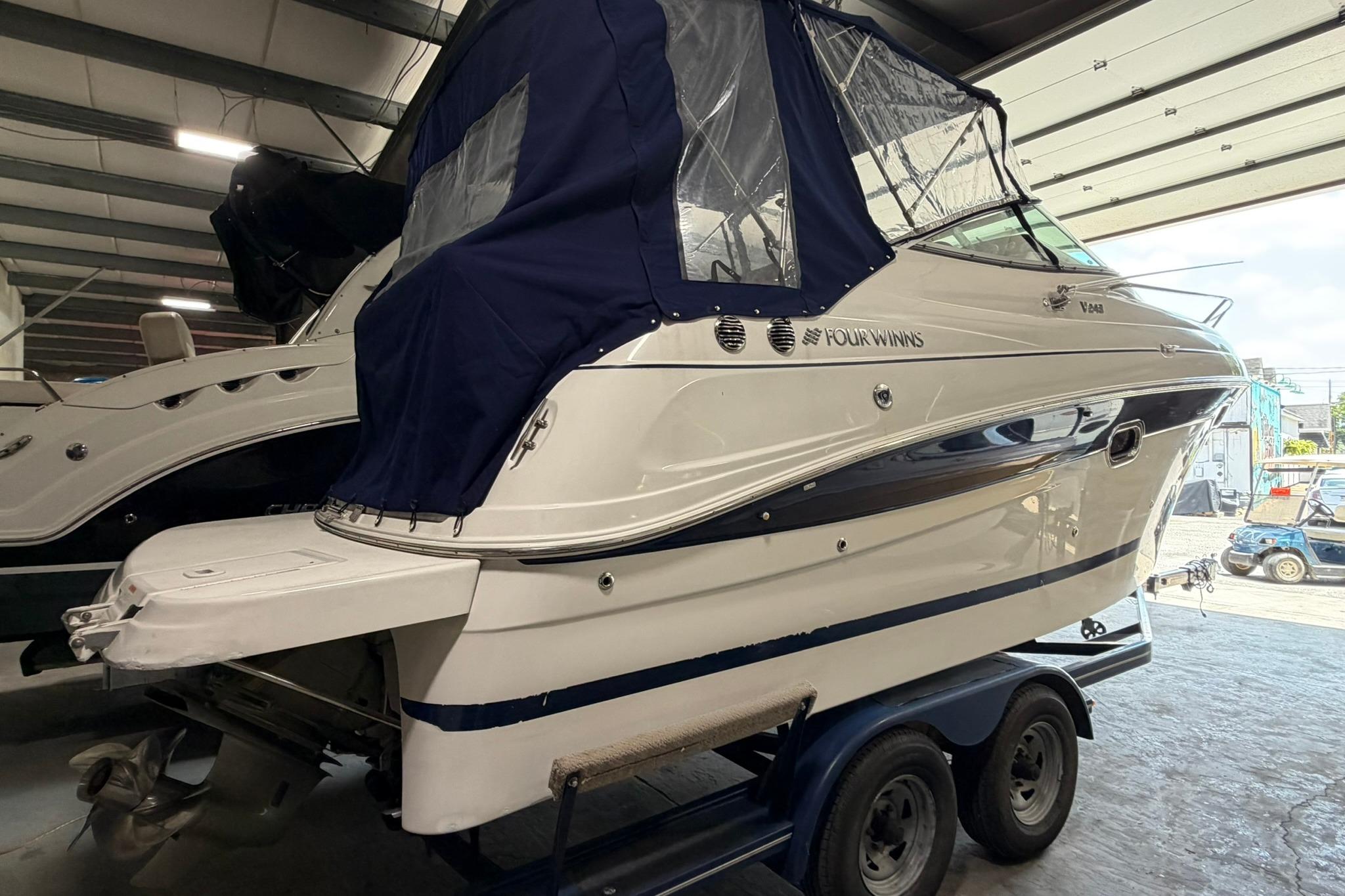 2008 Four Winns V248 boat with blue cover on trailer in storage facility.