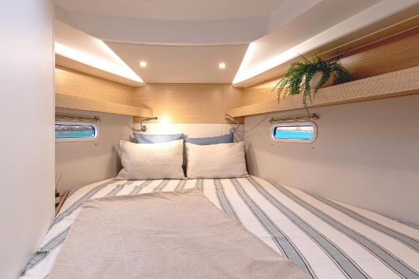 Cozy cabin interior of 2025 Hanse 360 yacht with striped bedding and porthole windows.