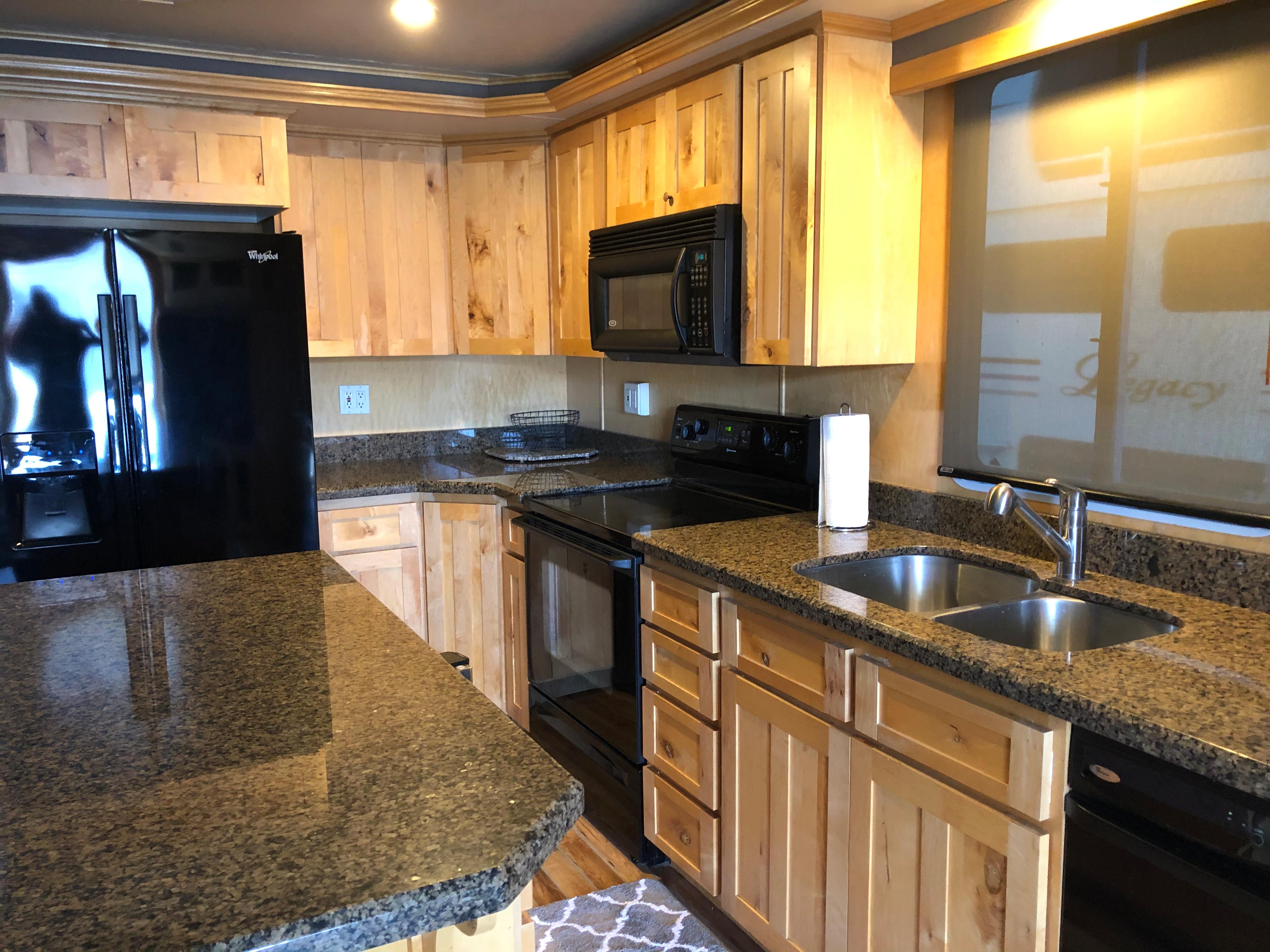Modern kitchen with granite countertops, wooden cabinets, black appliances, and double sink. Custom model: The Entourage Shares #21,33 and 40