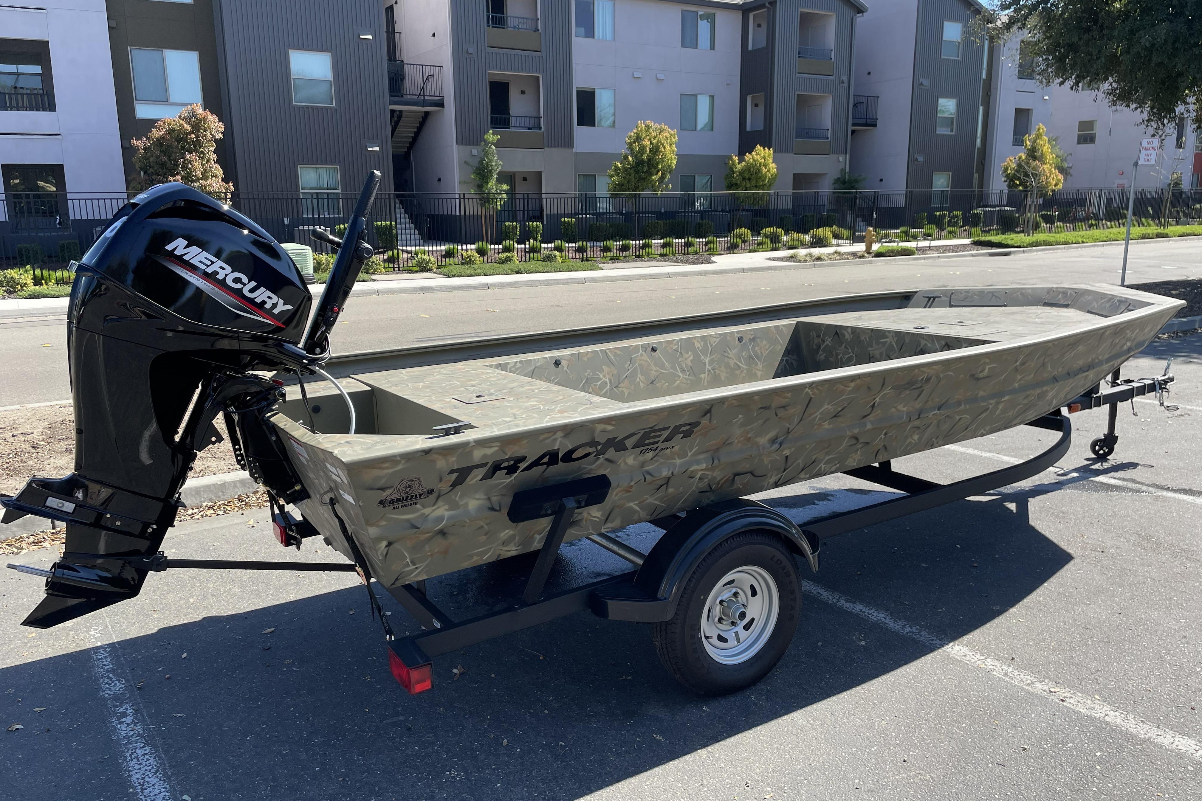 2025 Tracker Grizzly 1754 Jon boat with Mercury engine on trailer, parked outdoors.