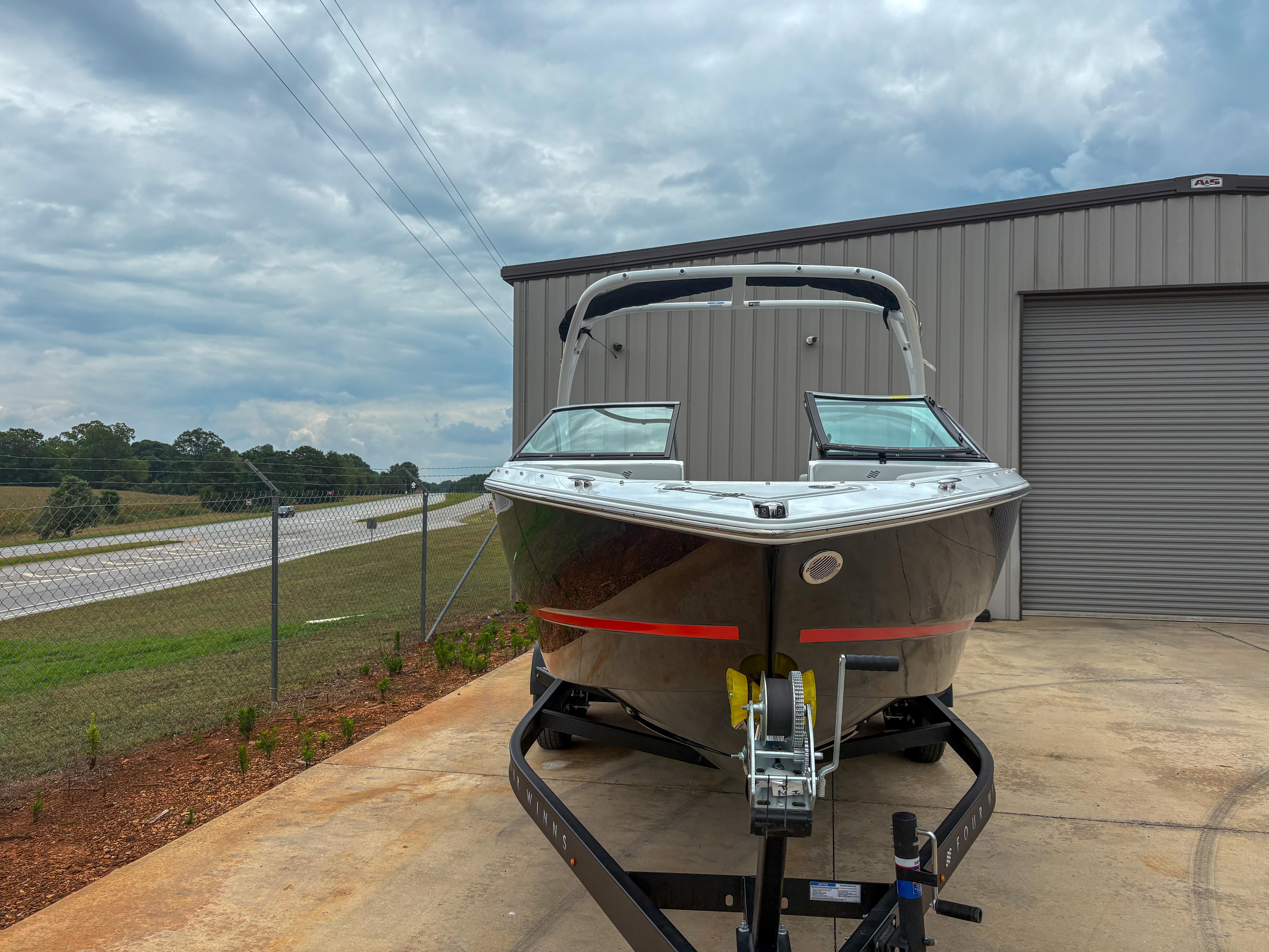 2026 Four Winns H2 Freedom boat on trailer, parked near a metal building under cloudy skies.