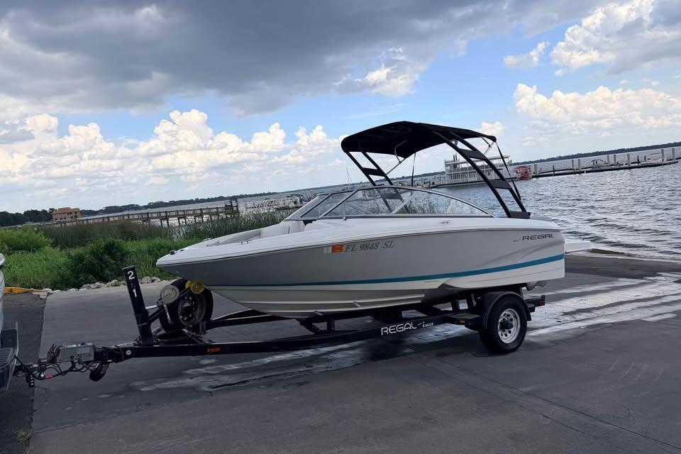 2019 Regal 1900 ES Bowrider on trailer by waterfront under cloudy sky.