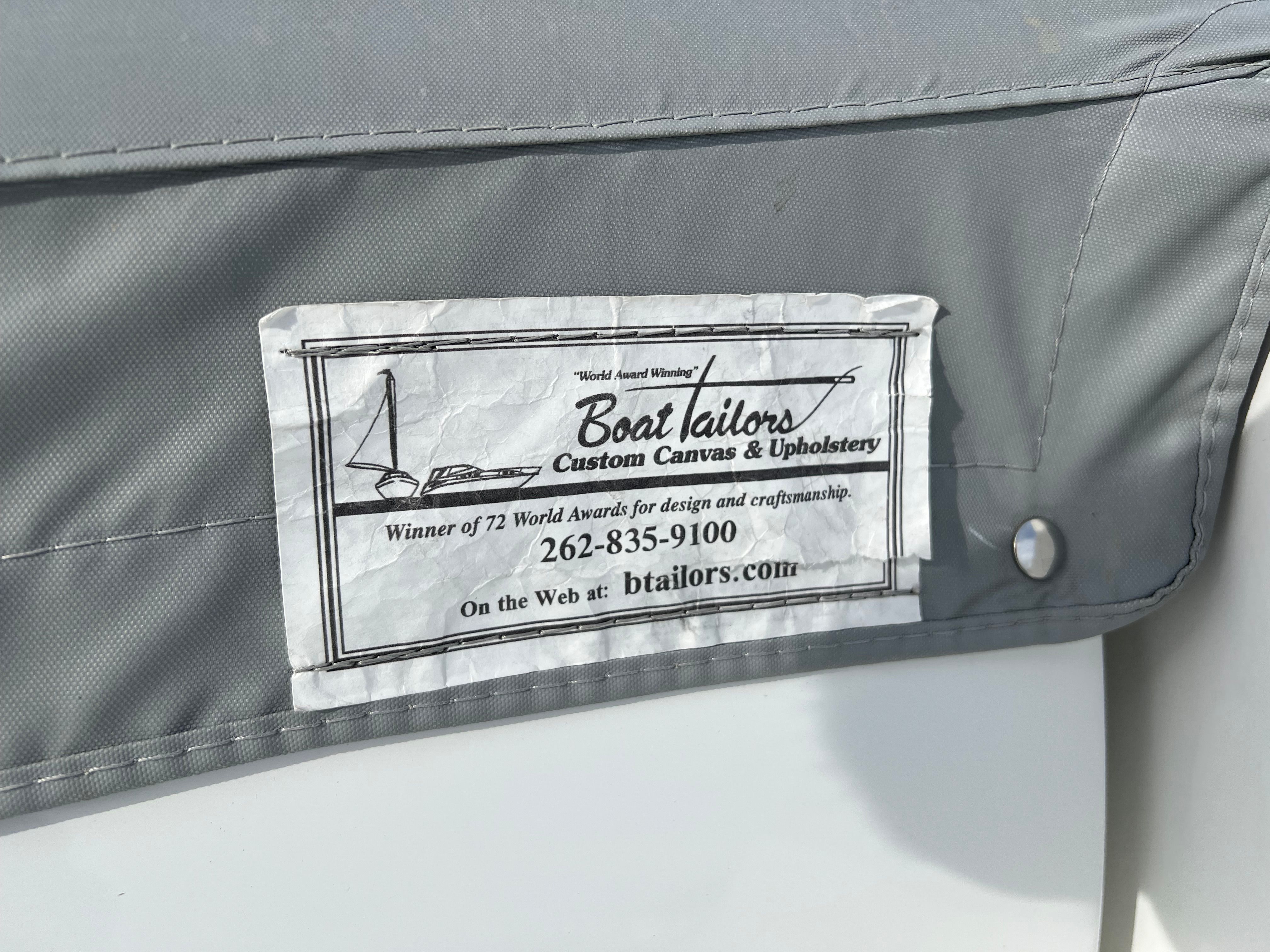 A gray boat cover with a "Boat Tailors" label for custom canvas and upholstery work.