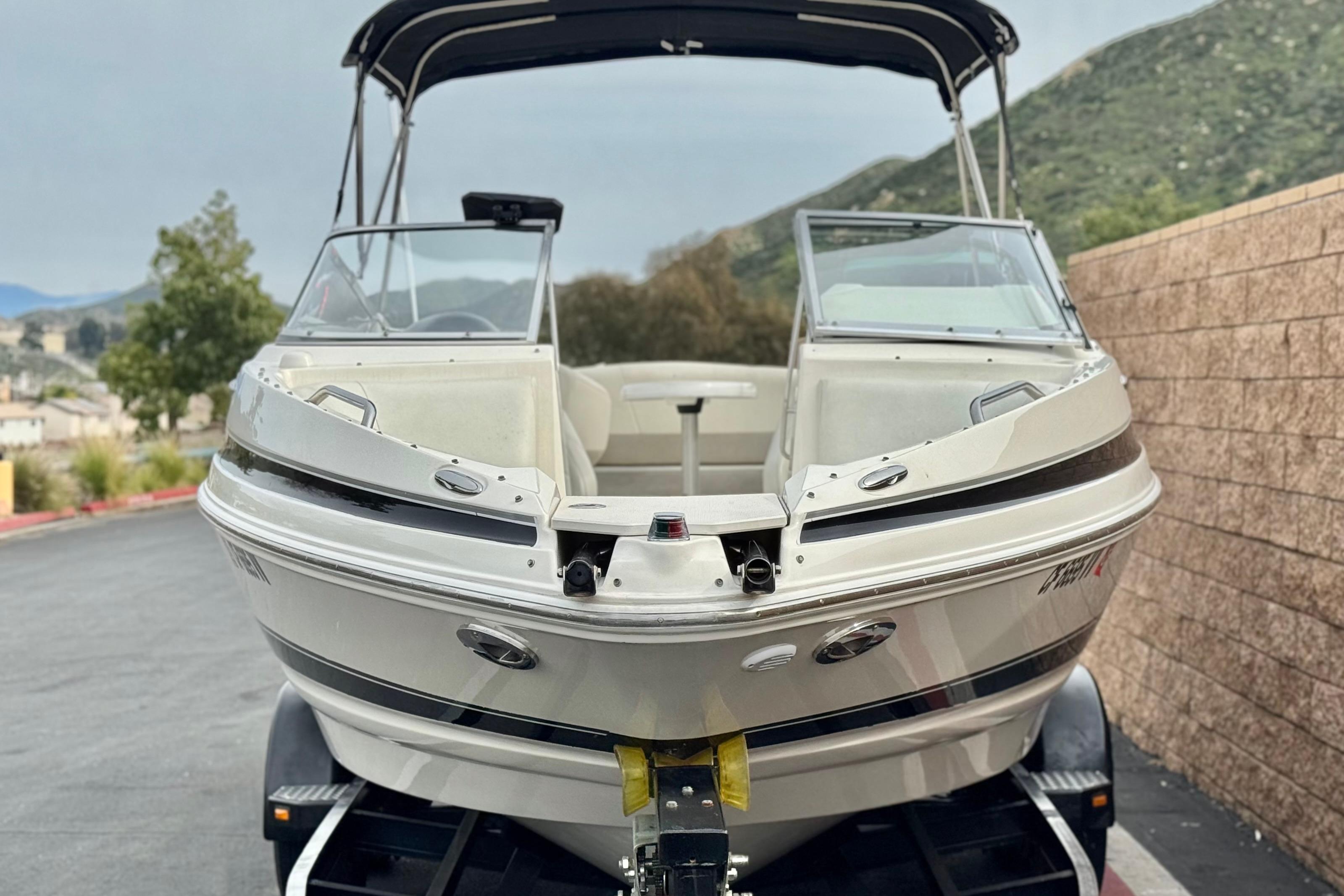 2006 Larson LXi 248 boat on trailer, parked outdoors with scenic background.