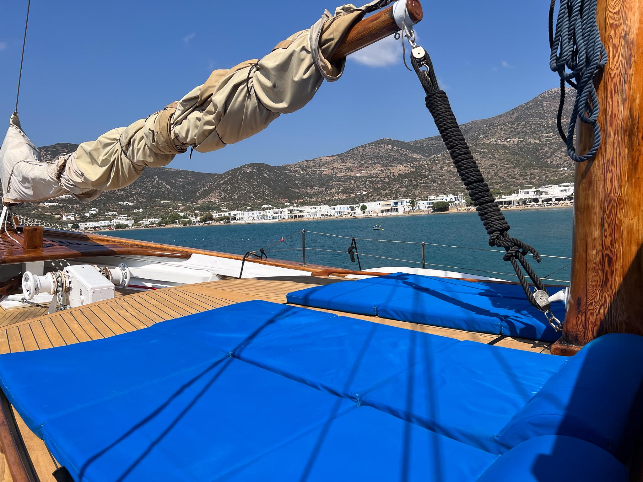 Wooden deck of 1969 Psarros Shipyard yacht with blue cushions, coastal view.