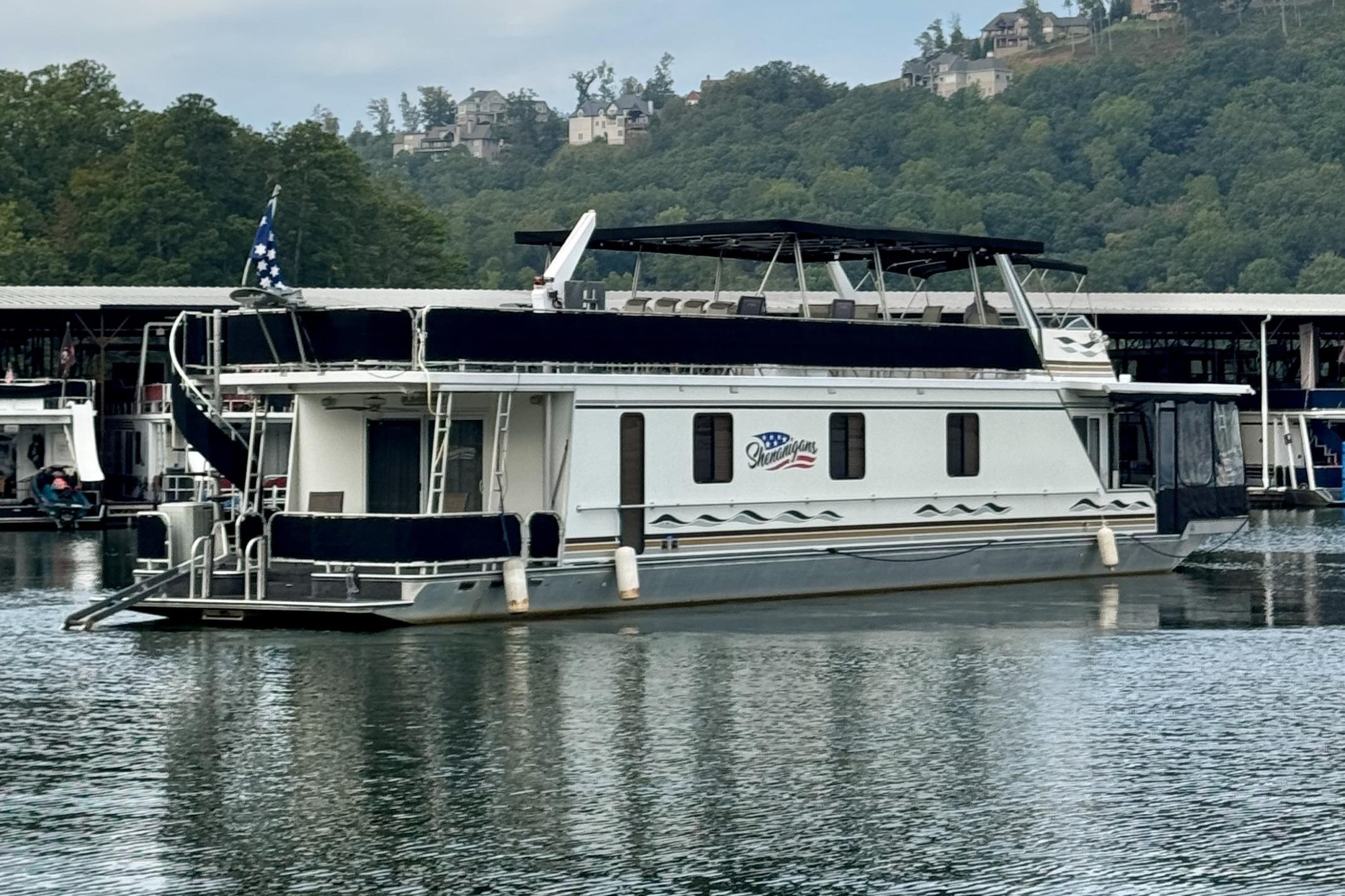 1998 Sumerset 16x76 houseboat docked on a serene lake with lush green hills.