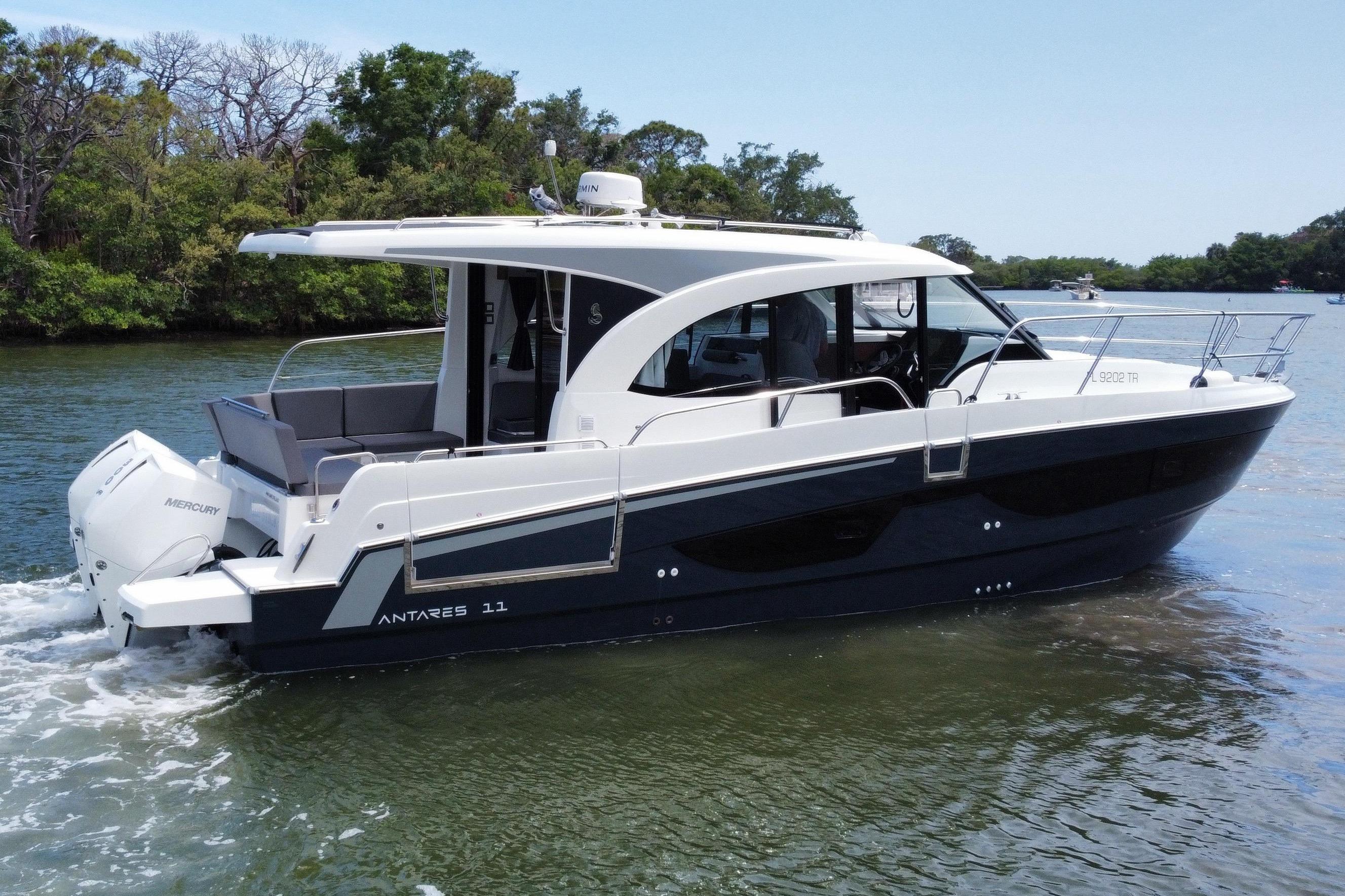 A 2024 Beneteau Antares 11 cruising on calm water, surrounded by trees.