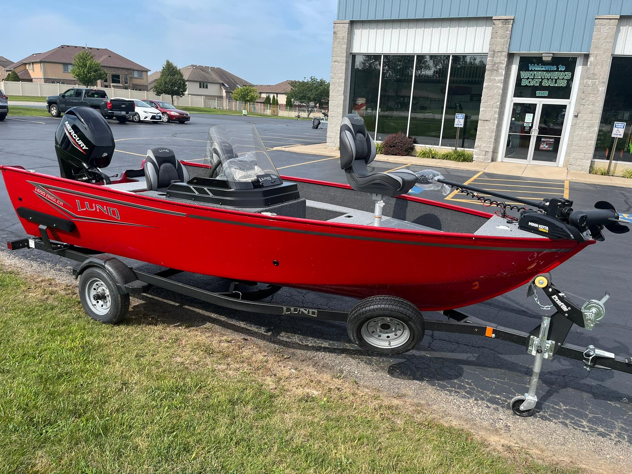 2026 Lund 1650 Angler SS boat in vibrant red on a trailer outside a dealership.