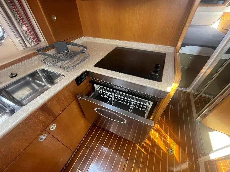 1985 Princess Sedan Flybridge kitchen with stove, sink, and dishwasher on wooden flooring.