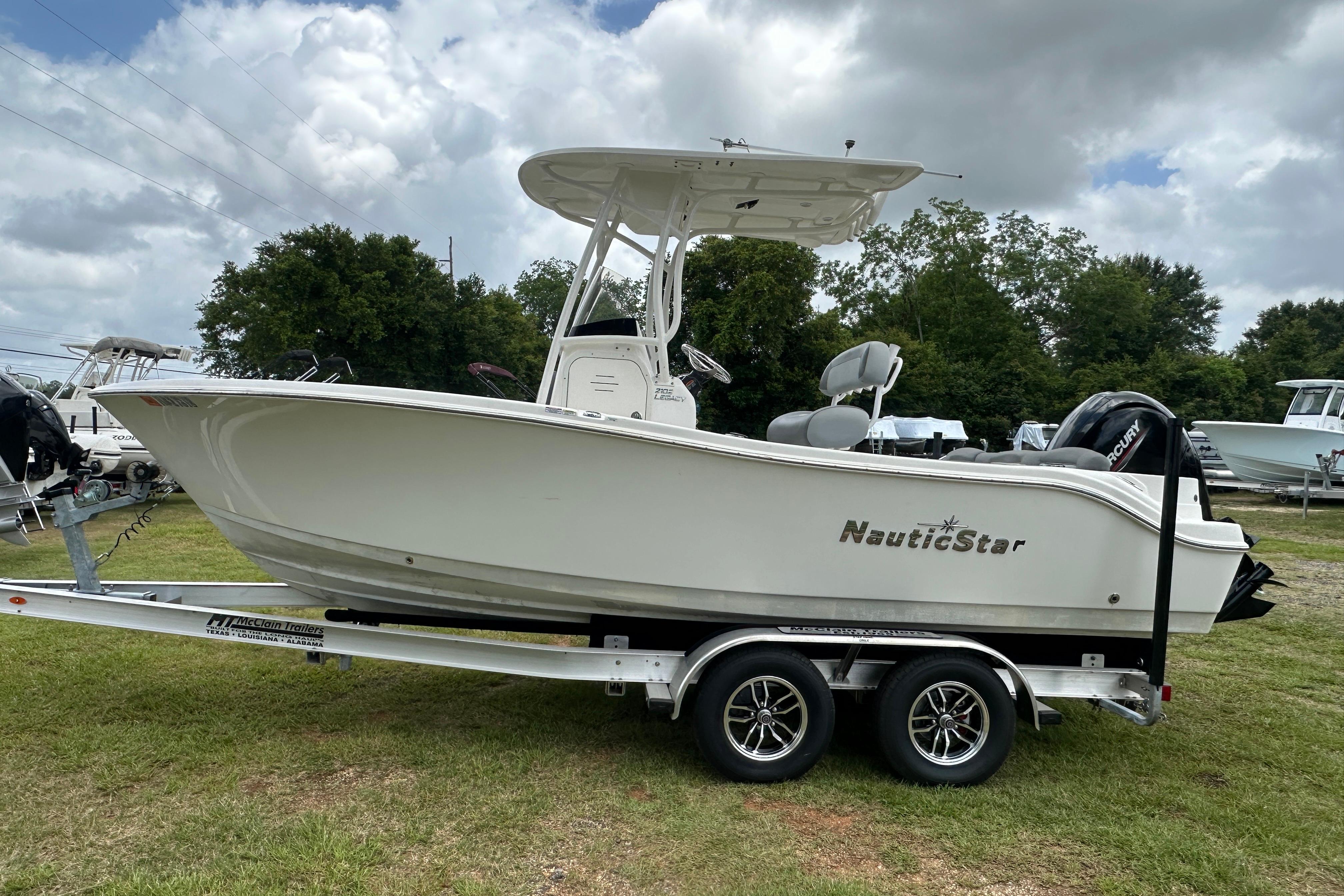 2023 NauticStar 2102 Legacy boat on trailer, parked on grass under cloudy sky.