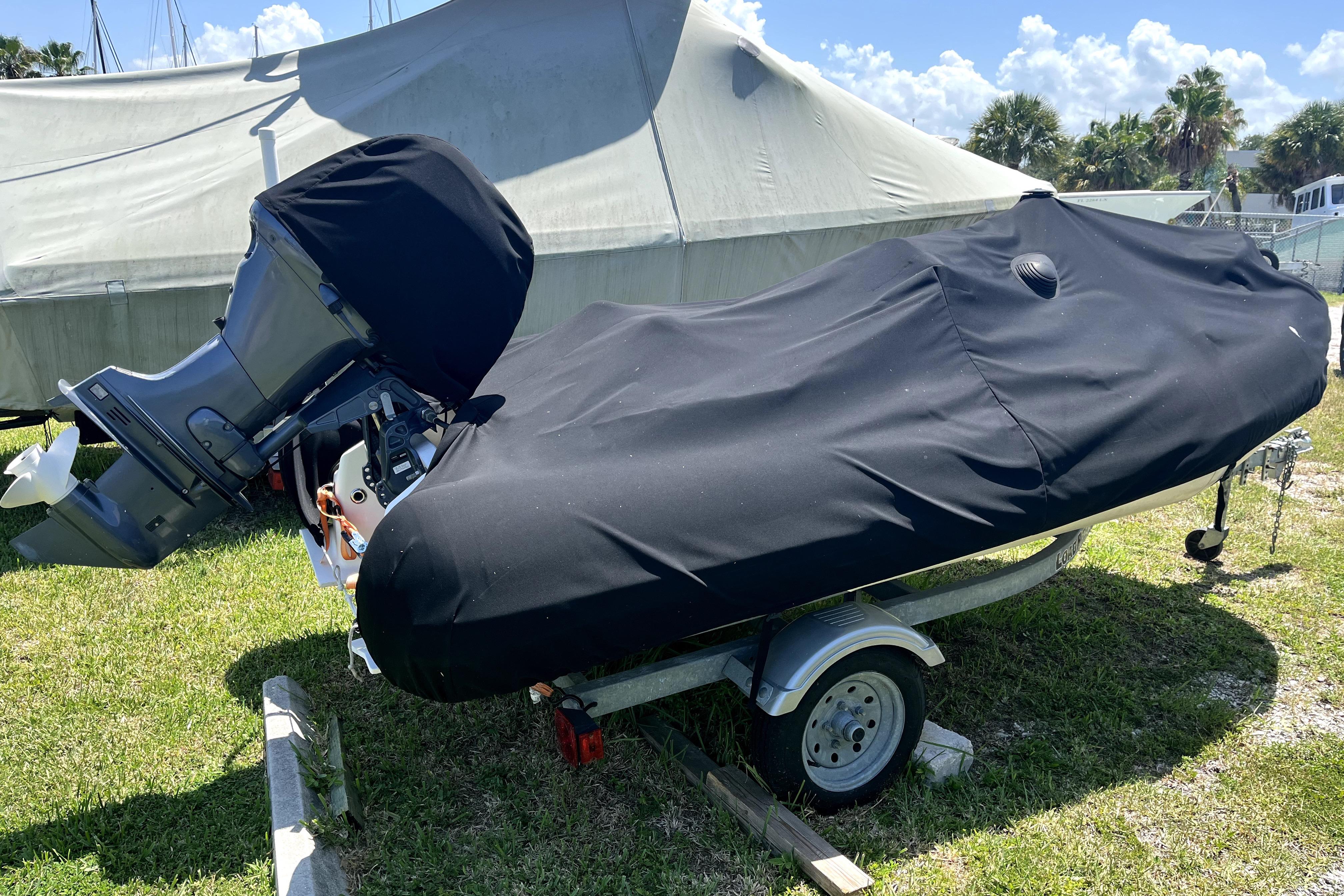 A covered boat on a trailer, parked on grass under a sunny sky.