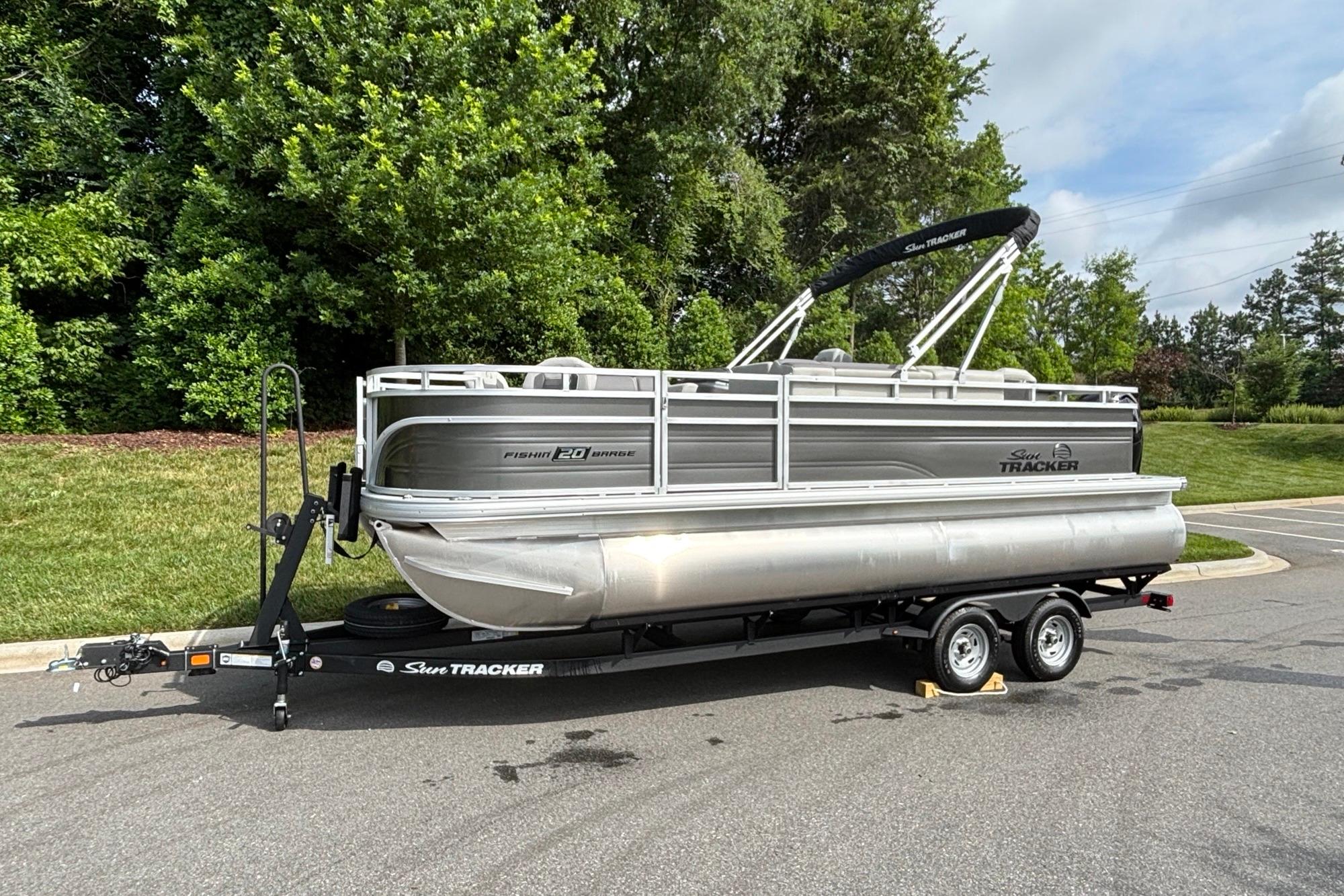 2026 Sun Tracker Fishin' Barge 20 DLX pontoon boat on trailer, parked outdoors.
