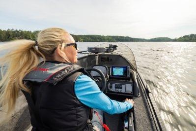Woman steering 2026 Alumacraft Escape 165 CS boat on a scenic lake.