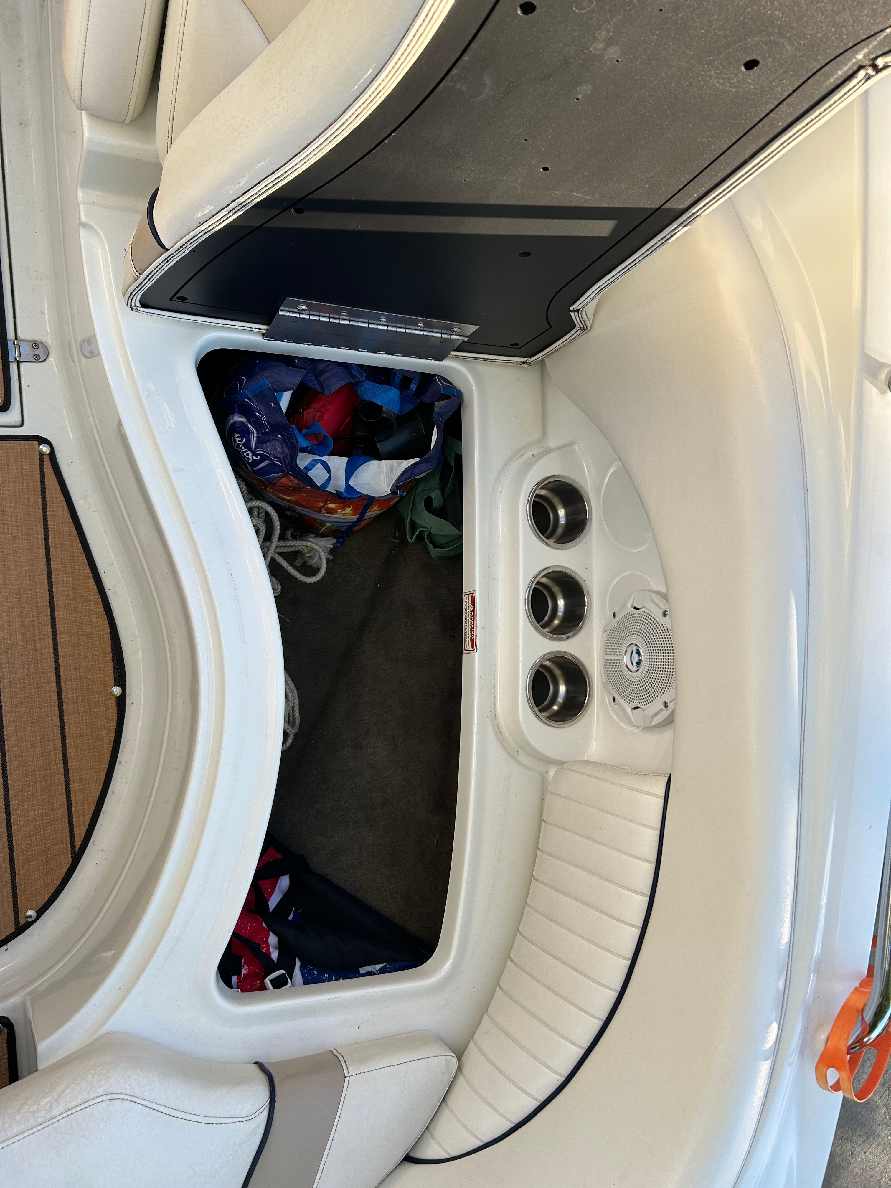 A boat with white upholstery, cup holders, and storage space containing ropes and towels.