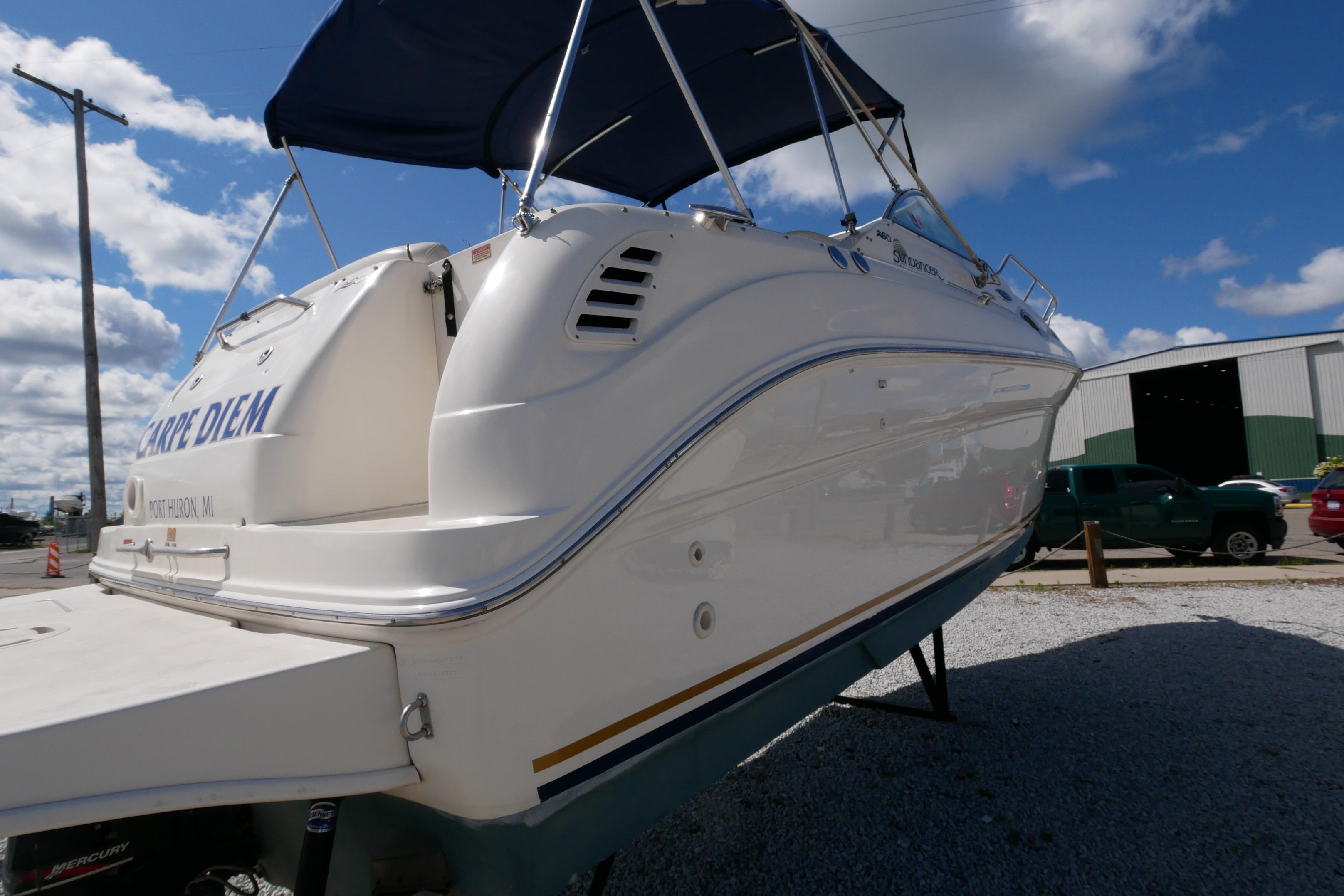 2003 Sea Ray 260 Sundancer boat with blue canopy, docked under a clear sky.
