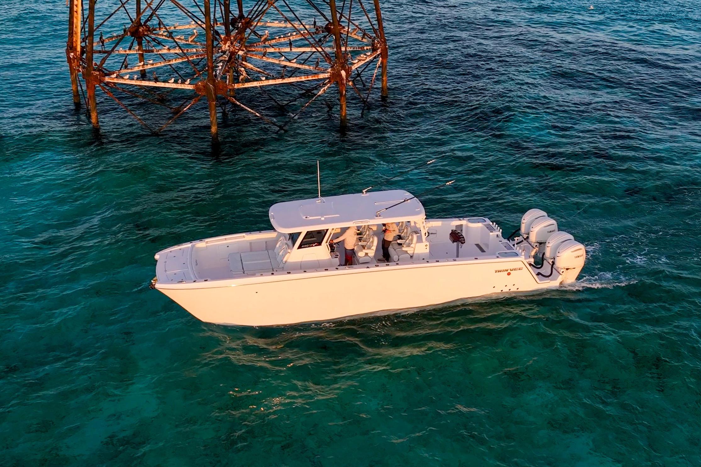 2026 Twin Vee 400 GFX2 CC boat cruising in clear turquoise waters near a metal structure.