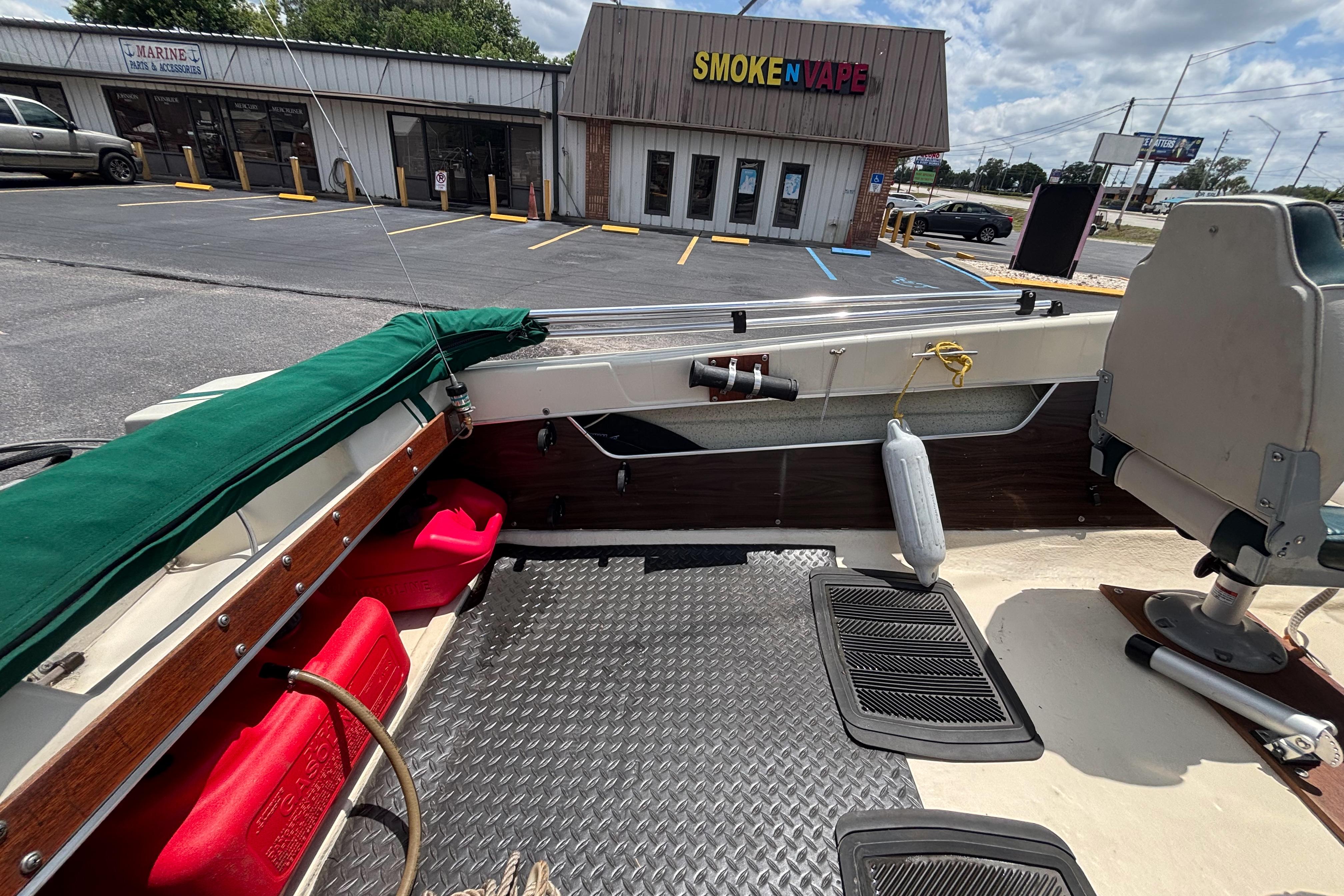 1966 Mohawk 15 boat interior with red fuel tanks, parked near a smoke shop.
