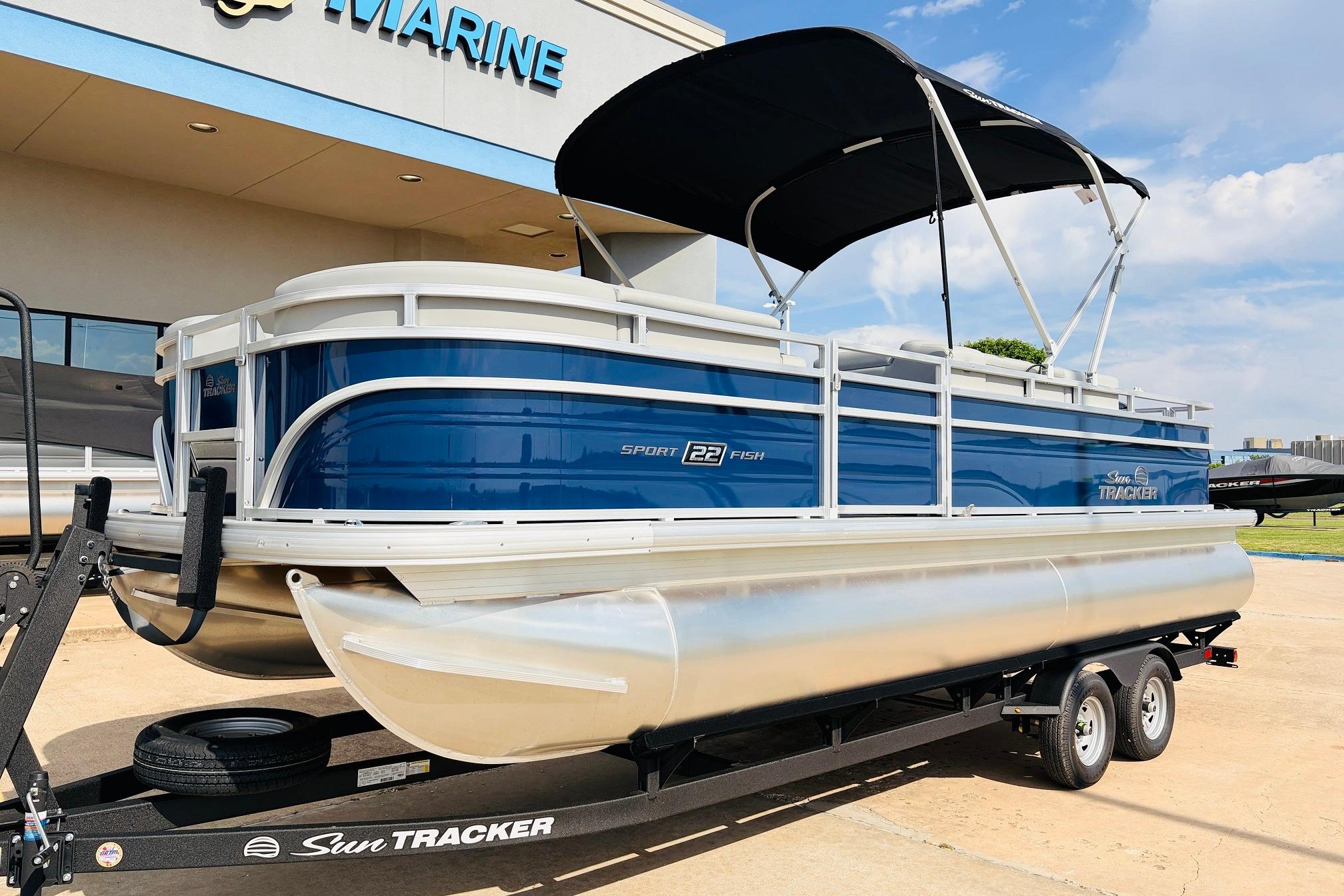 2026 Sun Tracker SportFish 22 DLX pontoon boat on trailer, parked outside marine dealership.