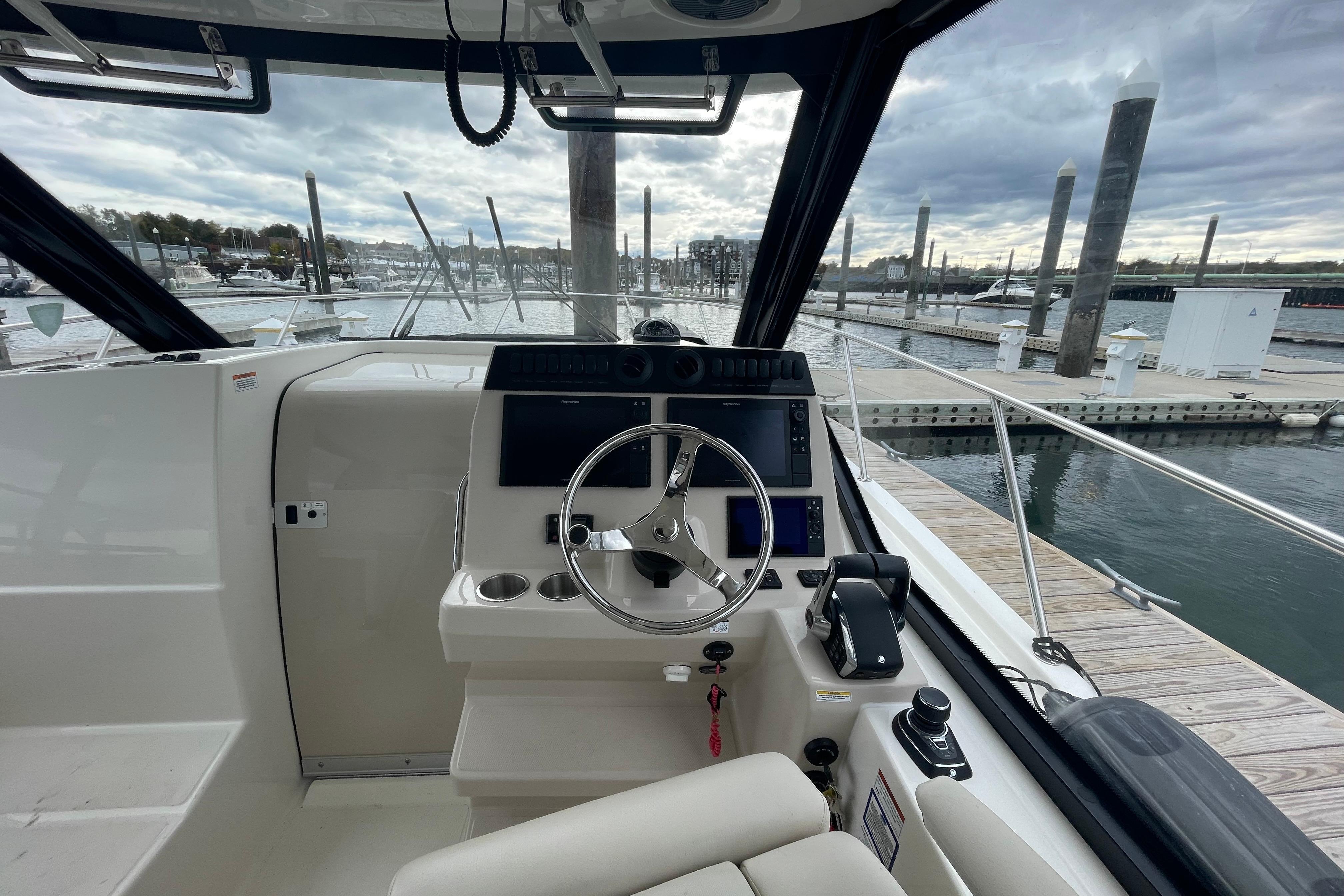 2023 Boston Whaler 325 Conquest helm with marina view, featuring modern controls and steering.