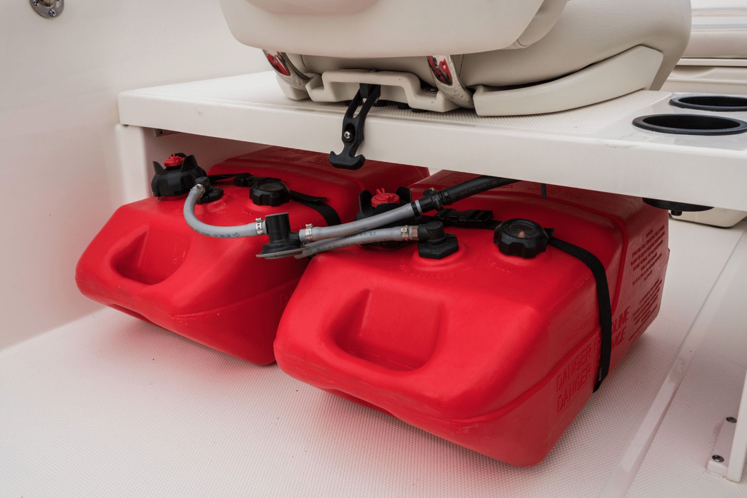 Two red fuel tanks are stored under a white seat on a boat.