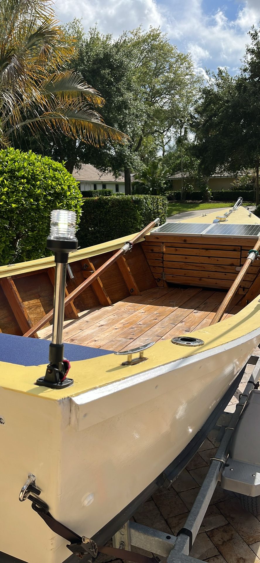A yellow dory boat with a wooden floor on a trailer, surrounded by trees.