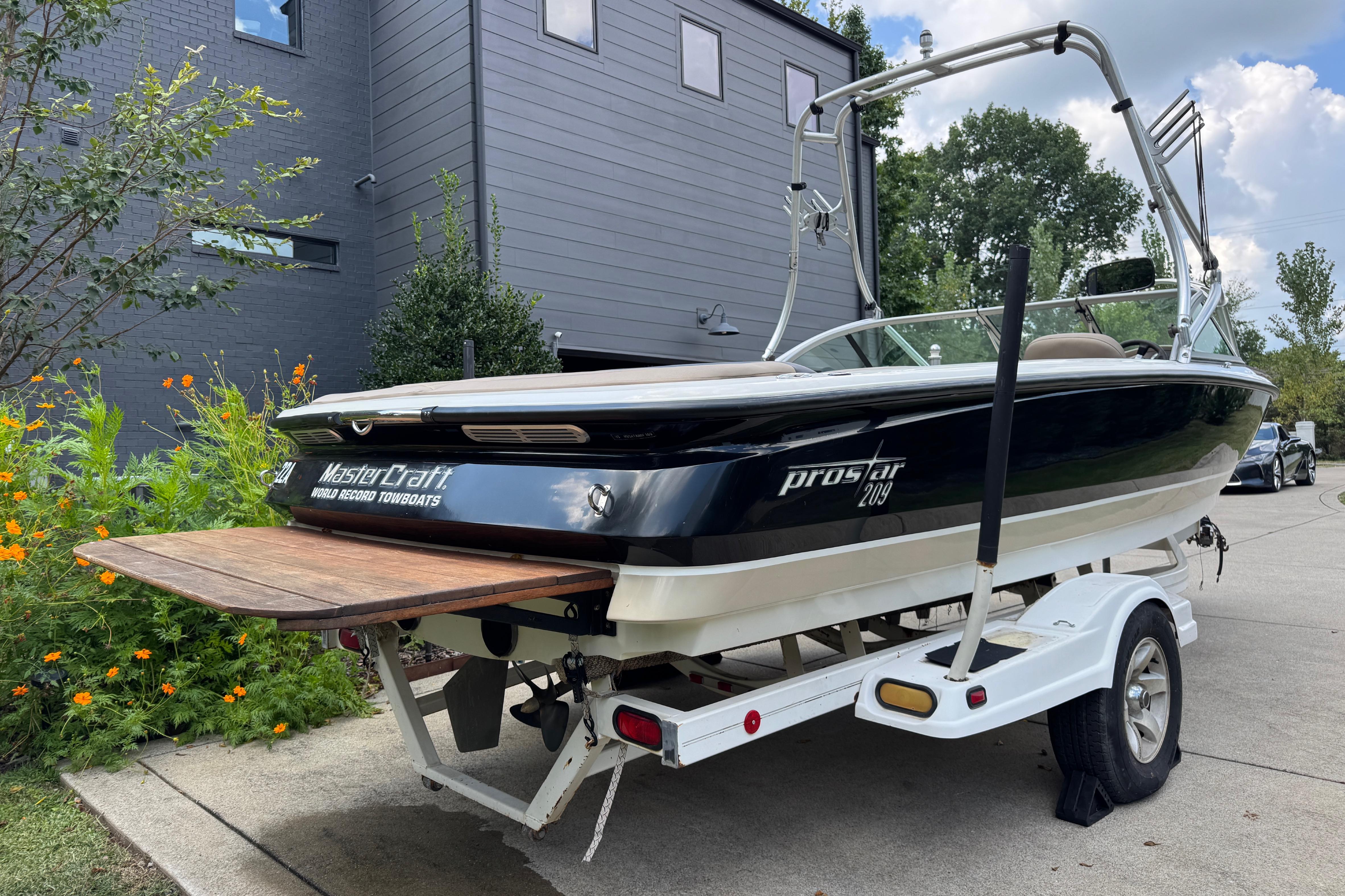 2002 MasterCraft ProStar 209 boat on trailer, parked near modern building.