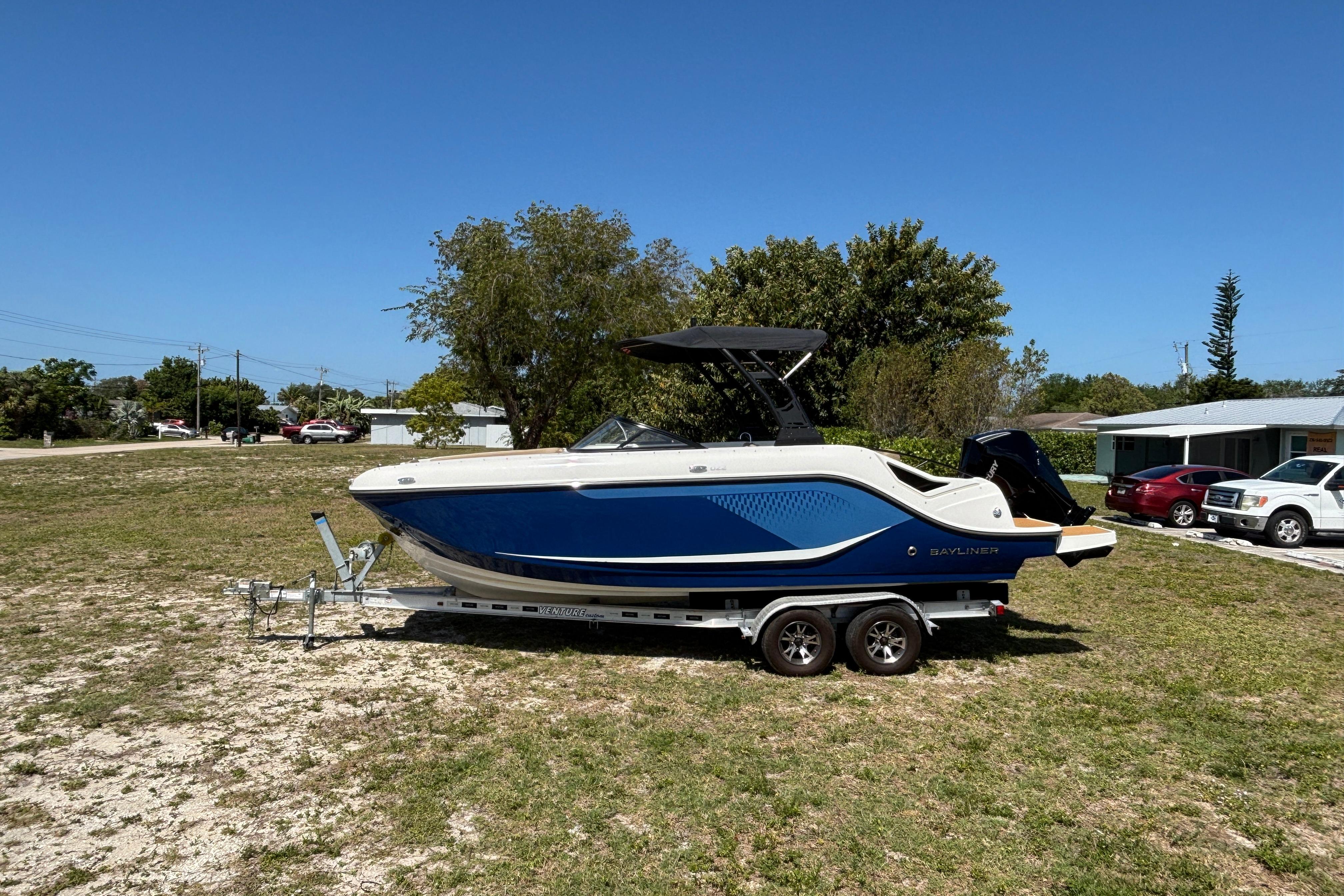 2026 Bayliner D22 boat on trailer, parked on grass under clear blue sky.