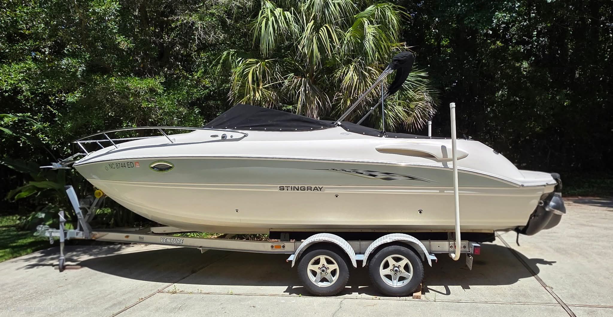 A white 2006 Stingray 250 CR boat on a trailer in a wooded area.