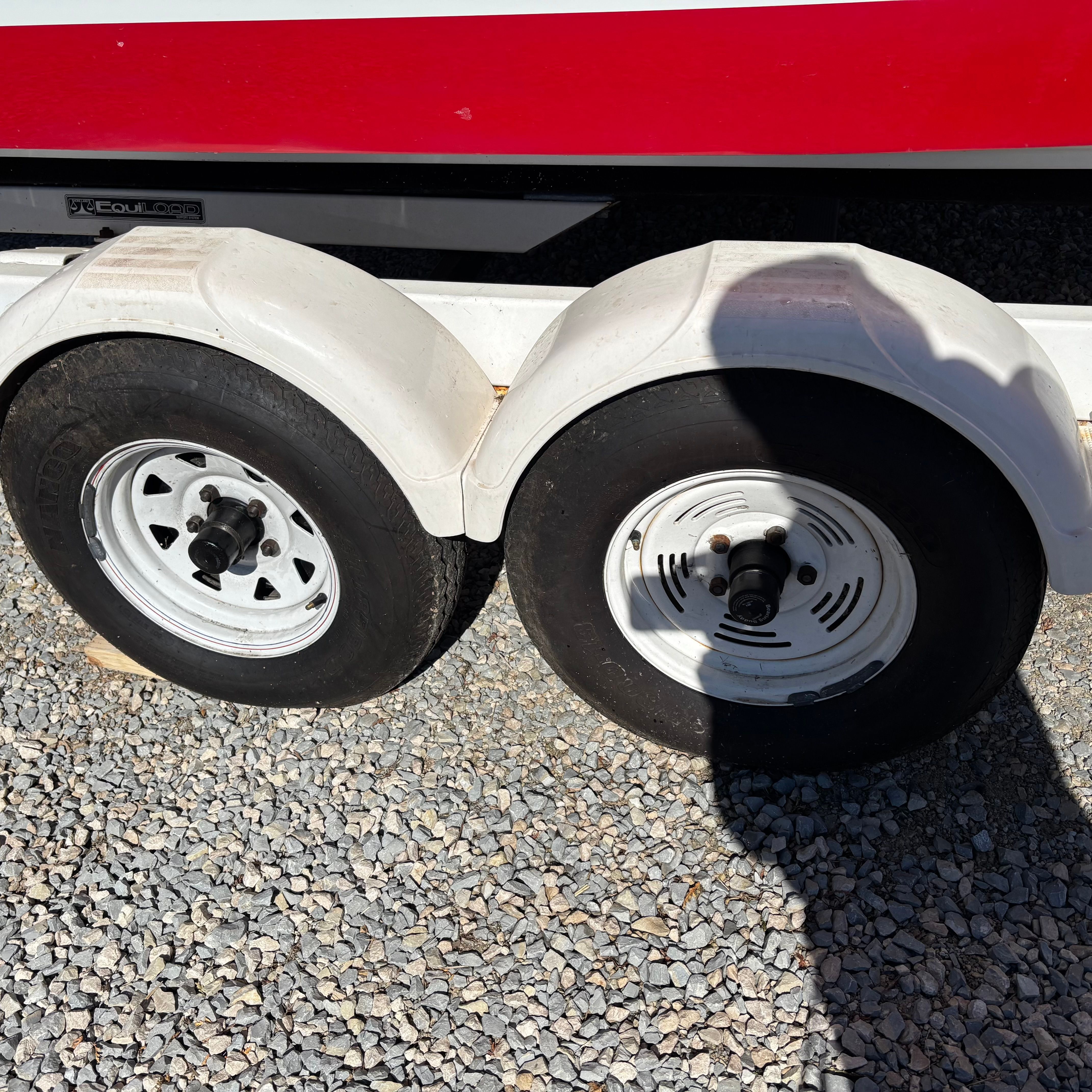 Close-up of a boat trailer with two white wheels on a gravel surface.